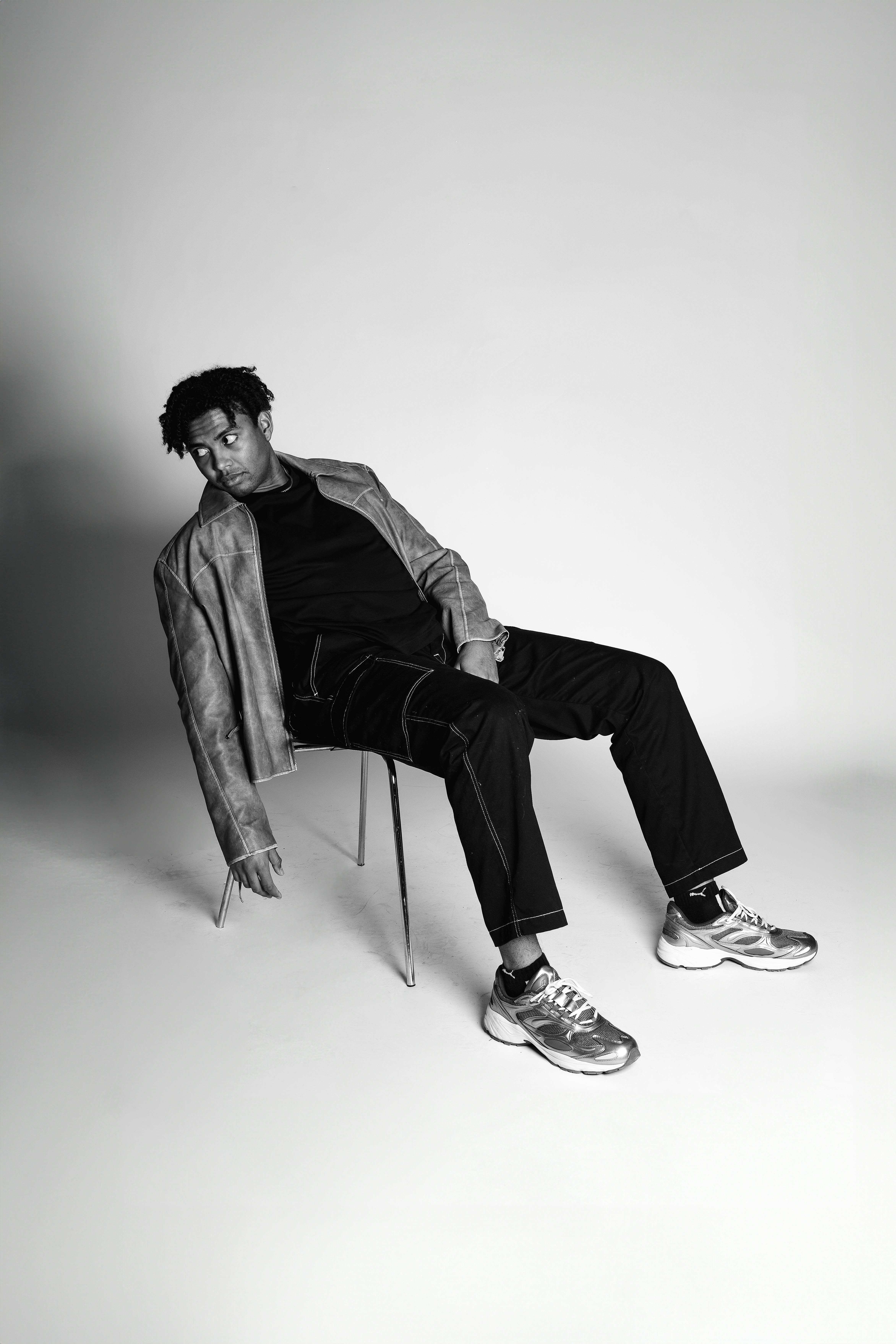 grátis Retrato monocromático de um homem com traje moderno, relaxado em uma cadeira, exalando estilo contemporâneo. Foto profissional