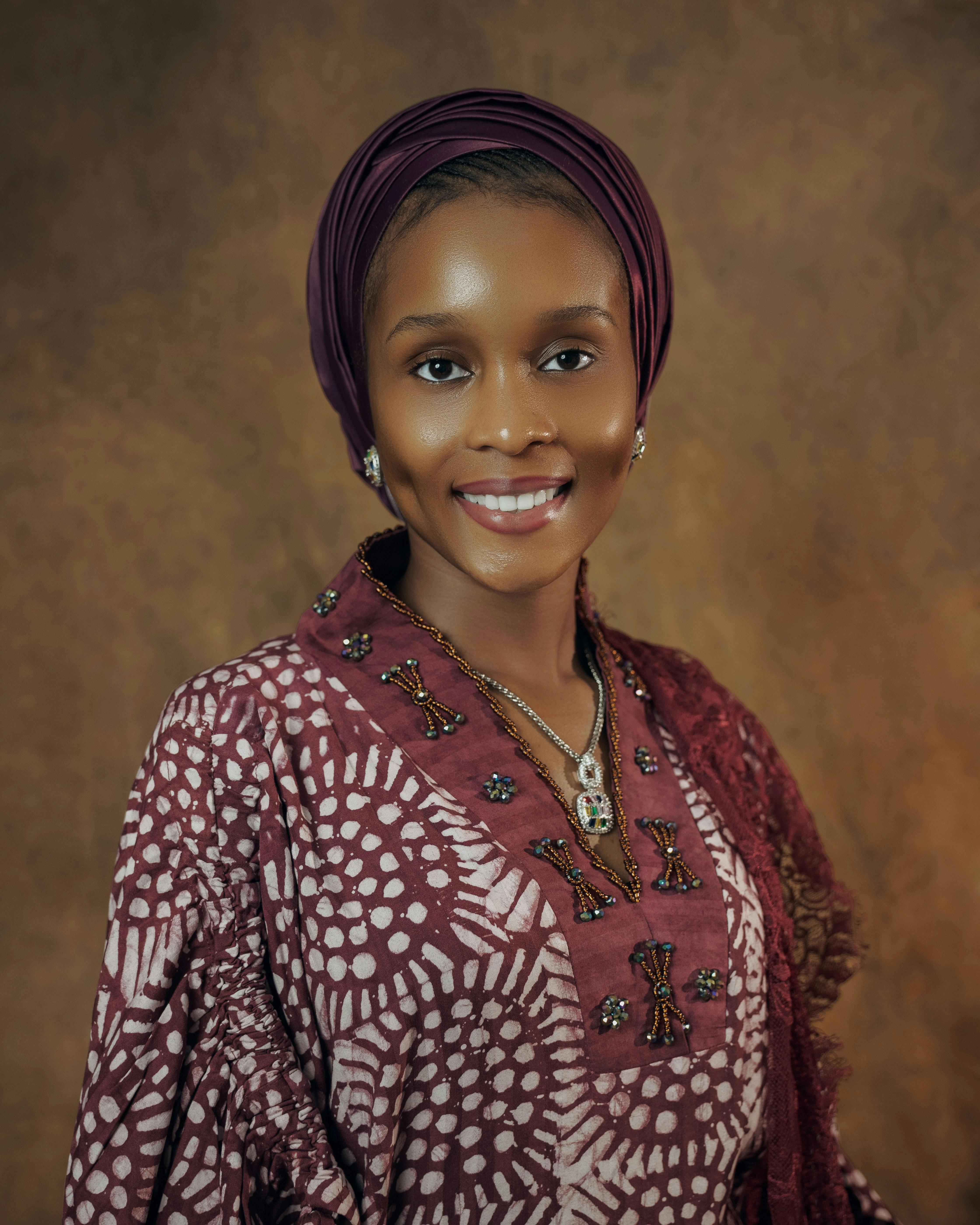 Portrait of an elegant woman in traditional African attire, smiling against a warm backdrop.