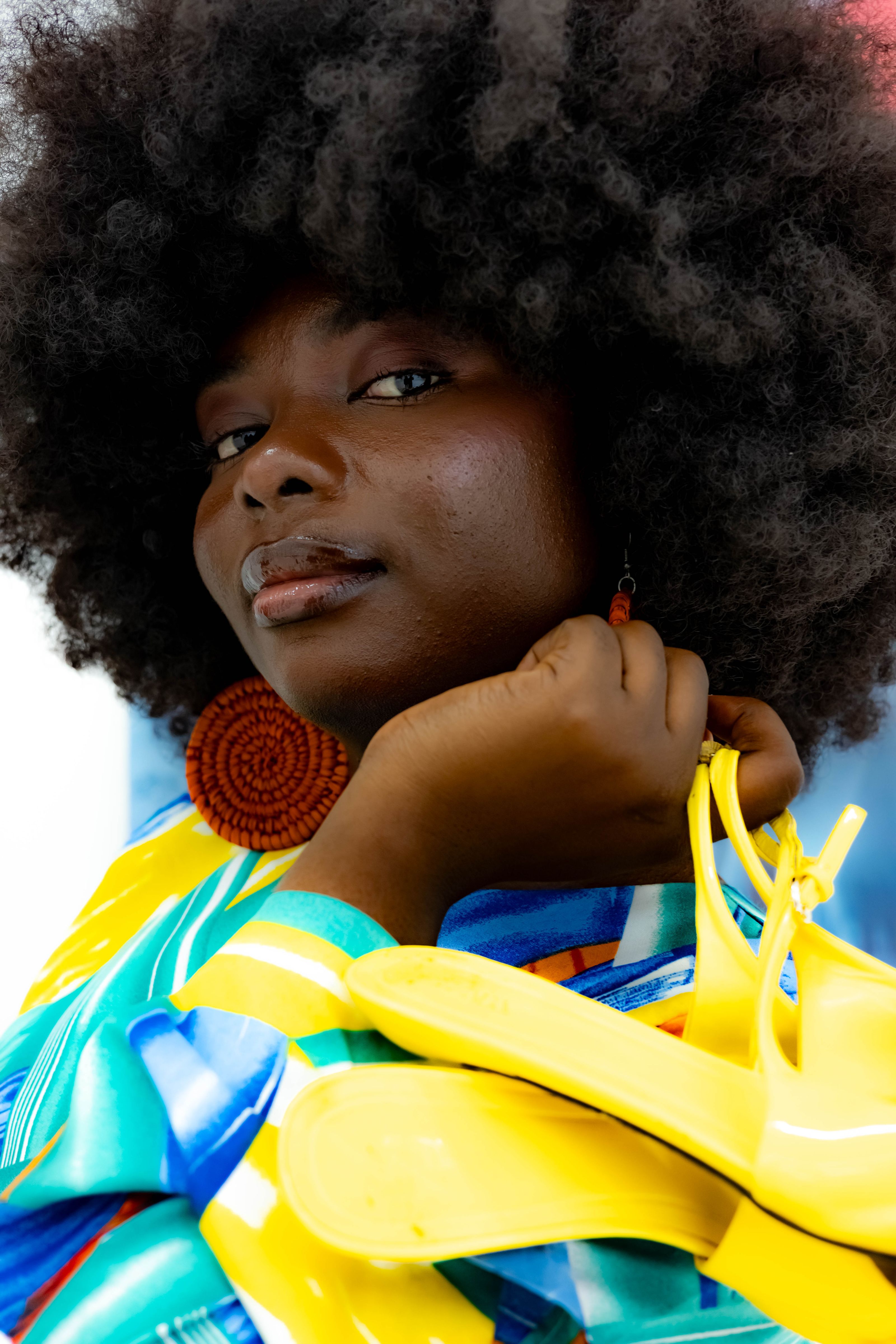 Um retrato elegante de uma mulher adulta com cabelo afro, brincos grandes e sandálias amarelas vibrantes.