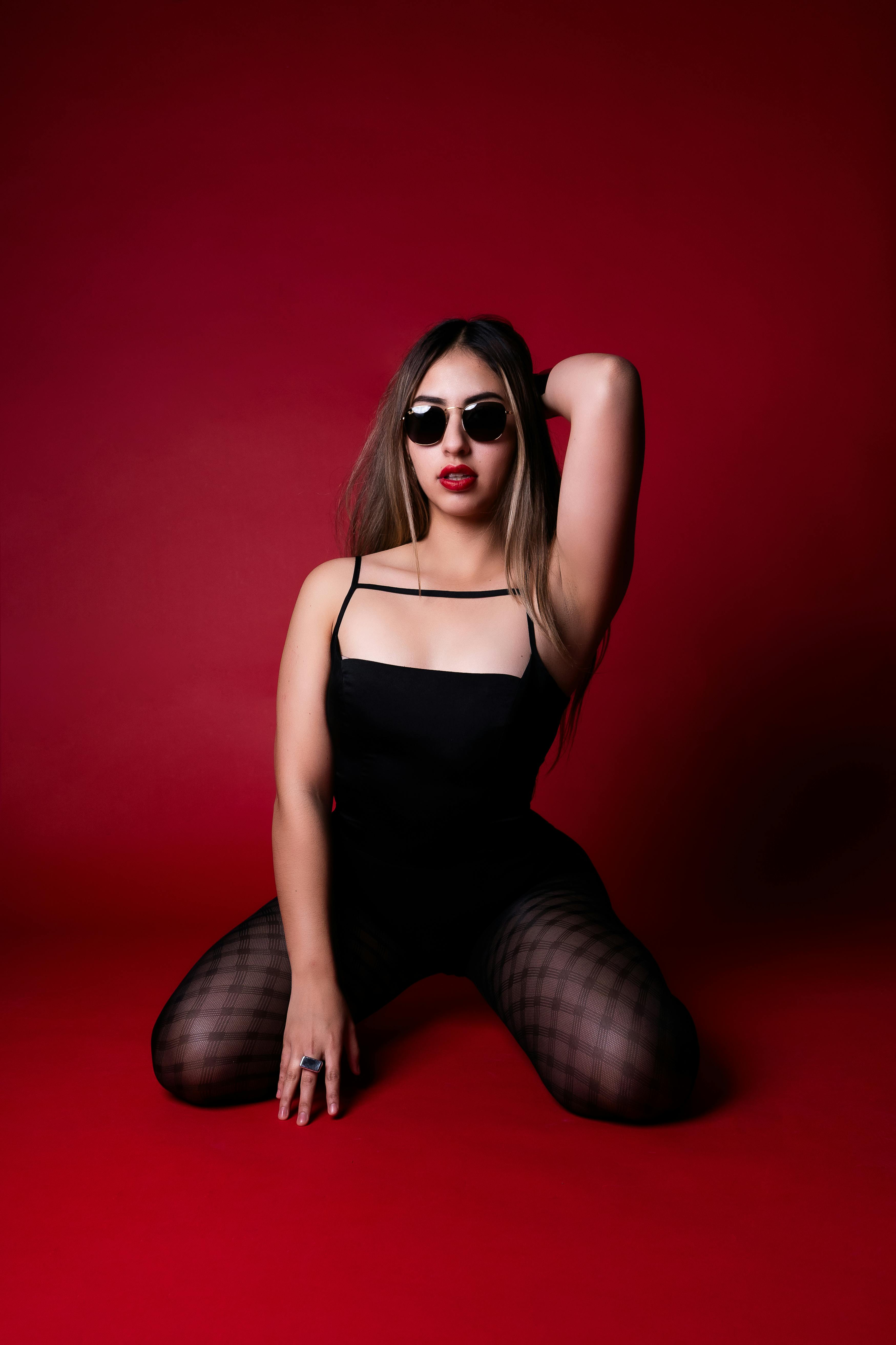 Gratis Slående kvinne poserer i svart antrekk mot en rød bakgrunn, utstråler selvtillit. Arkivbilde