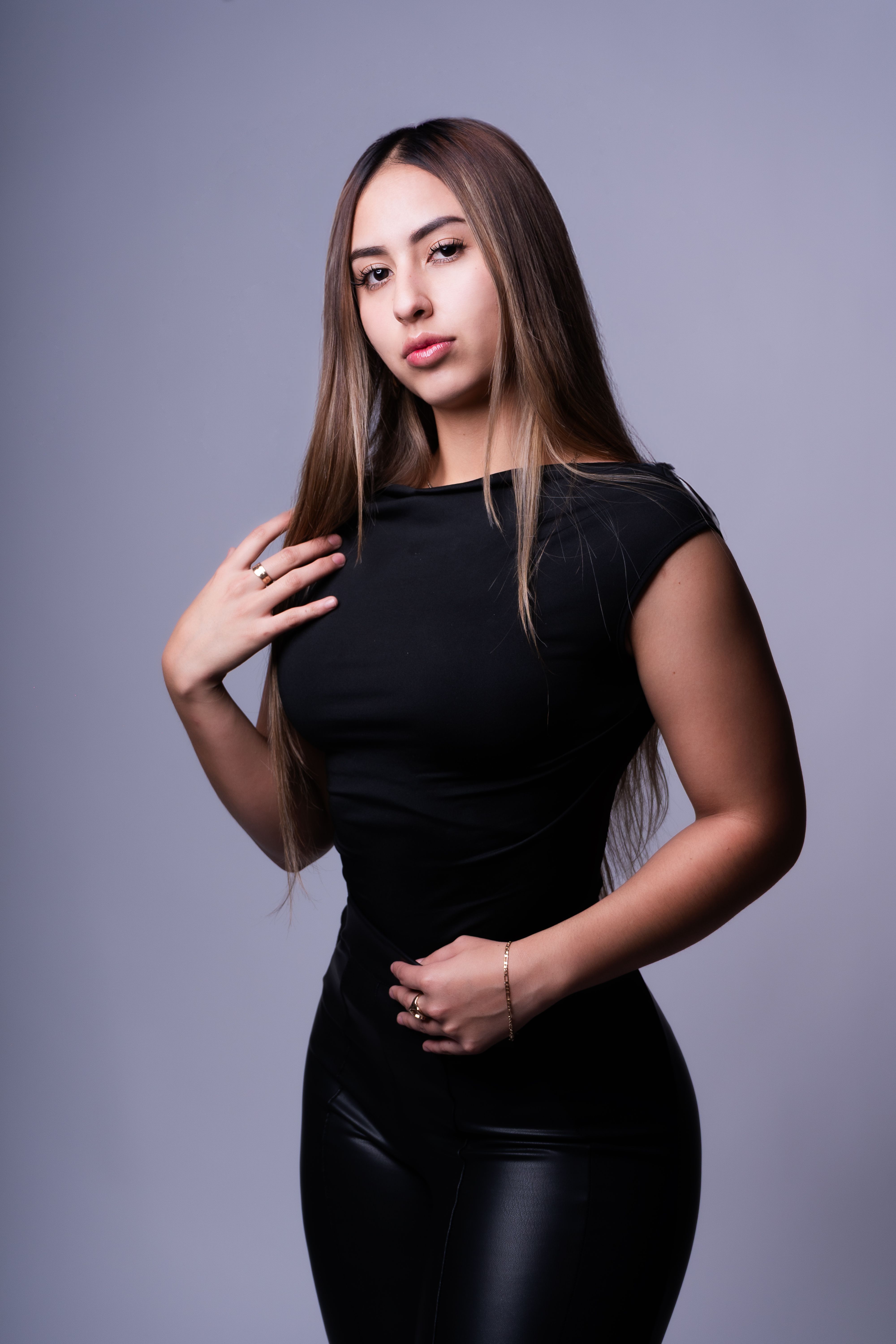 Stylish portrait of a confident young woman in a black outfit against a neutral background.