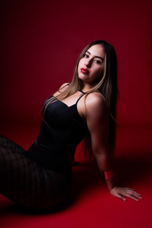 Free Elegant woman in black dress on red backdrop, exuding sensuality and confidence. Stock Photo