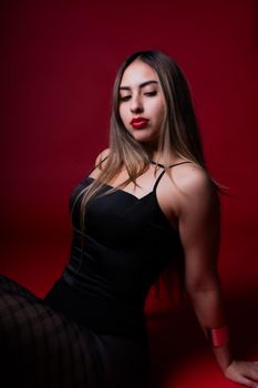 Stylish portrait of a woman in a black outfit against a deep red background, exuding confidence and elegance.