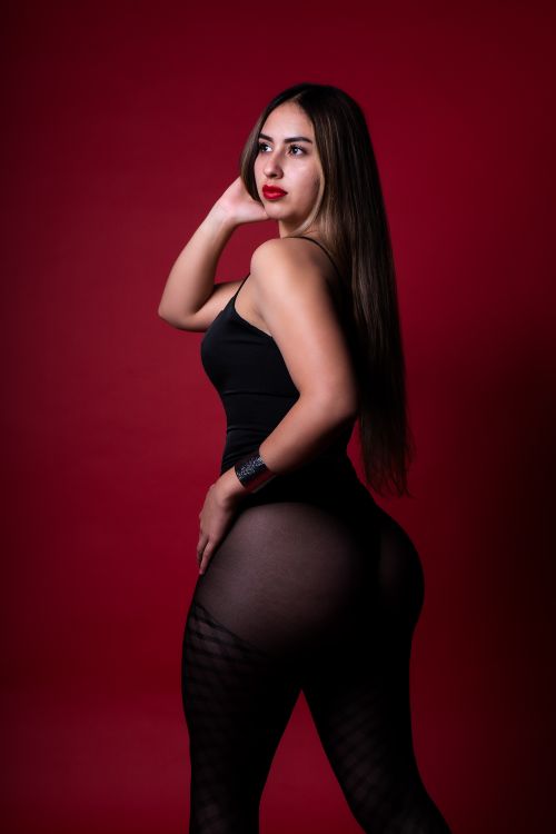 Free Elegant portrait of a woman in a sleek black outfit against a vibrant red backdrop. Stock Photo