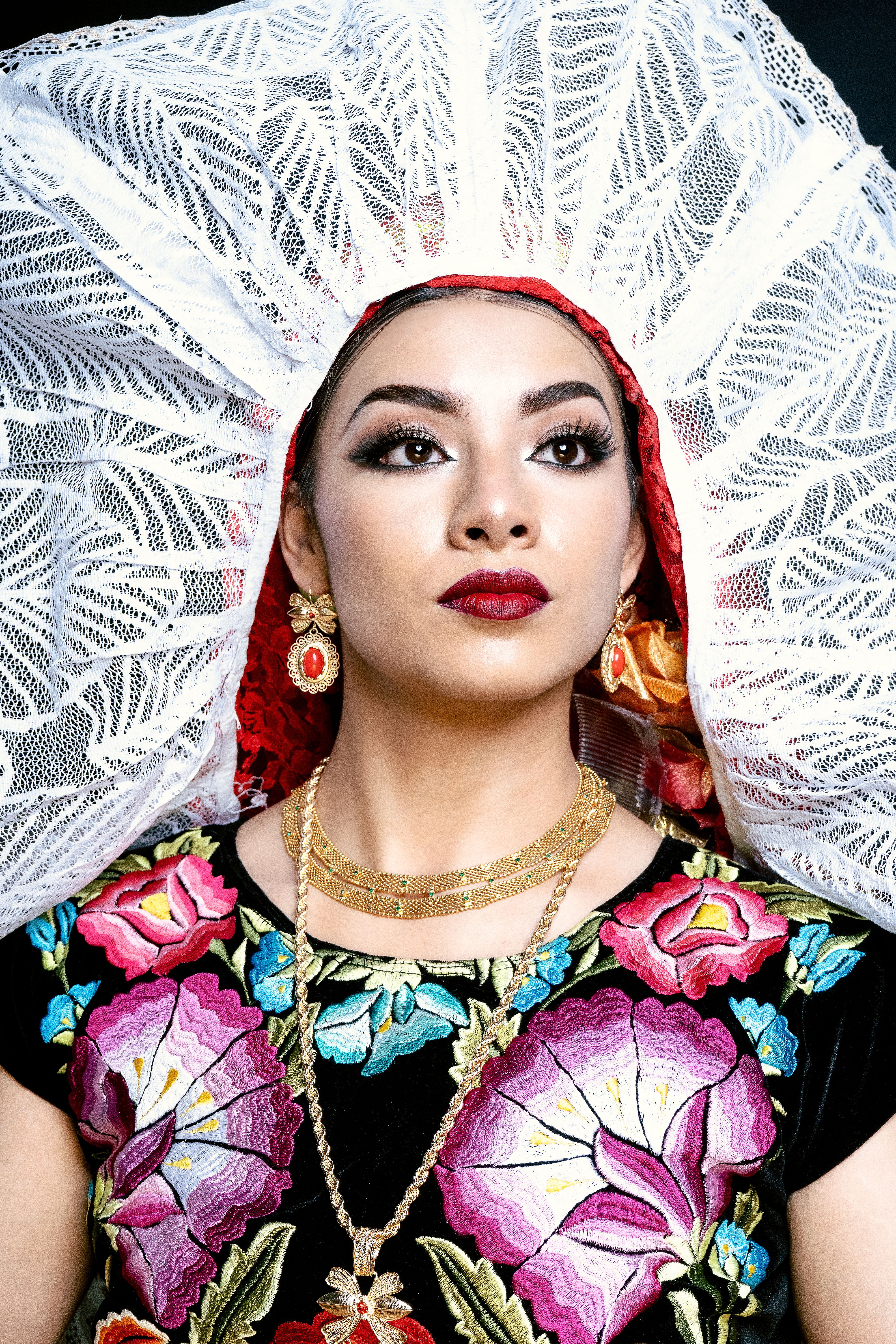 A portrait of a woman in vibrant Mexican traditional attire with ornate lace headpiece and floral embroidery.
