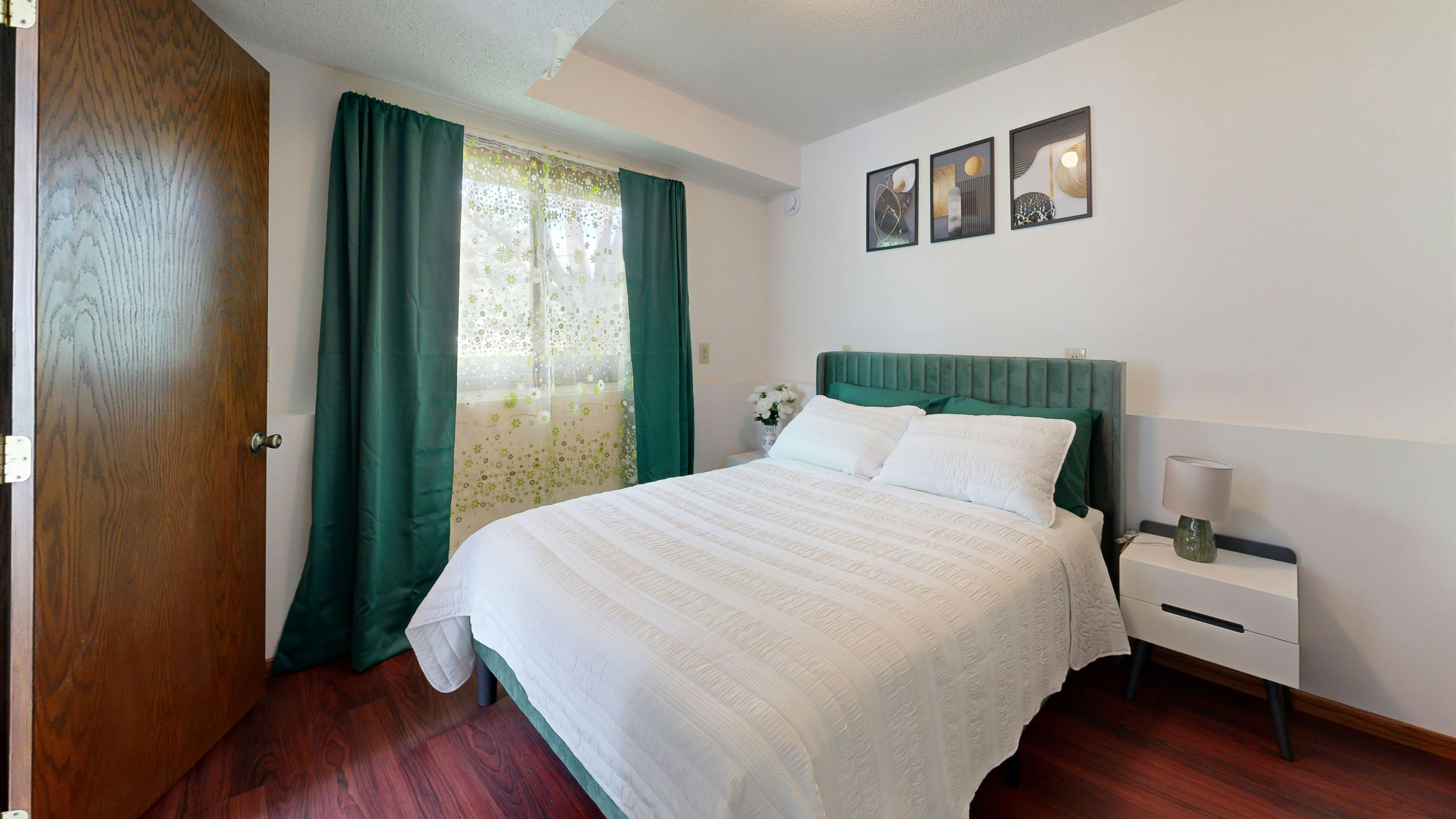 grátis Um quarto moderno e bem iluminado com cabeceira verde, lençóis brancos e obras de arte decorativas na parede. Foto profissional