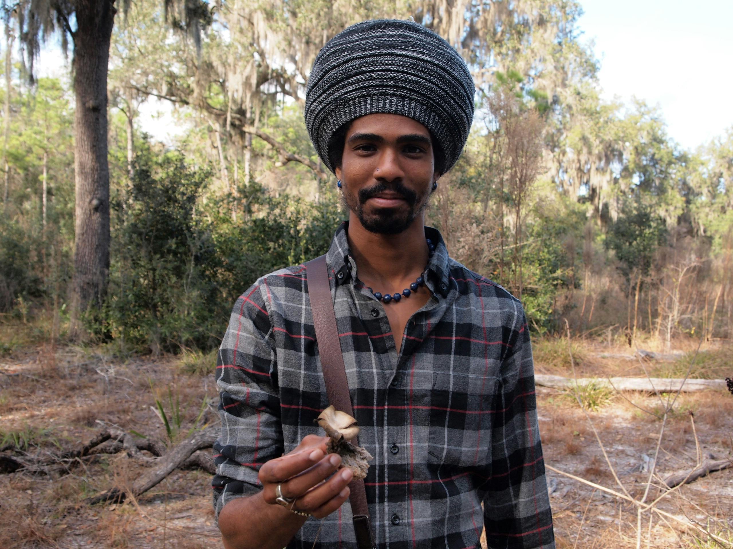 Man holding a mushroom while exploring a forest in Gainesville, Florida.