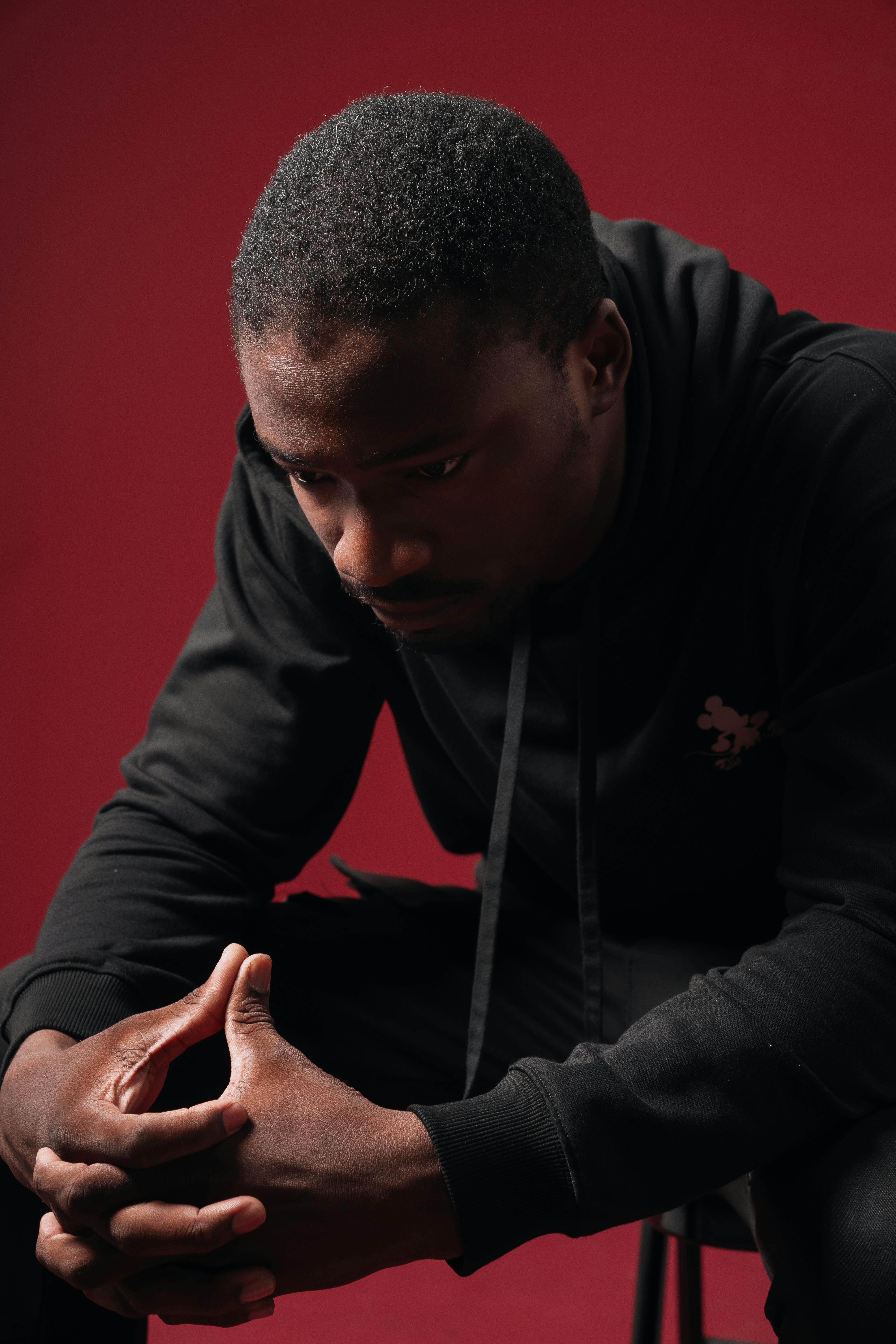 De franc Home pensatiu amb dessuadora amb caputxa negra sobre fons vermell, profundament reflexionat. Foto d'estoc