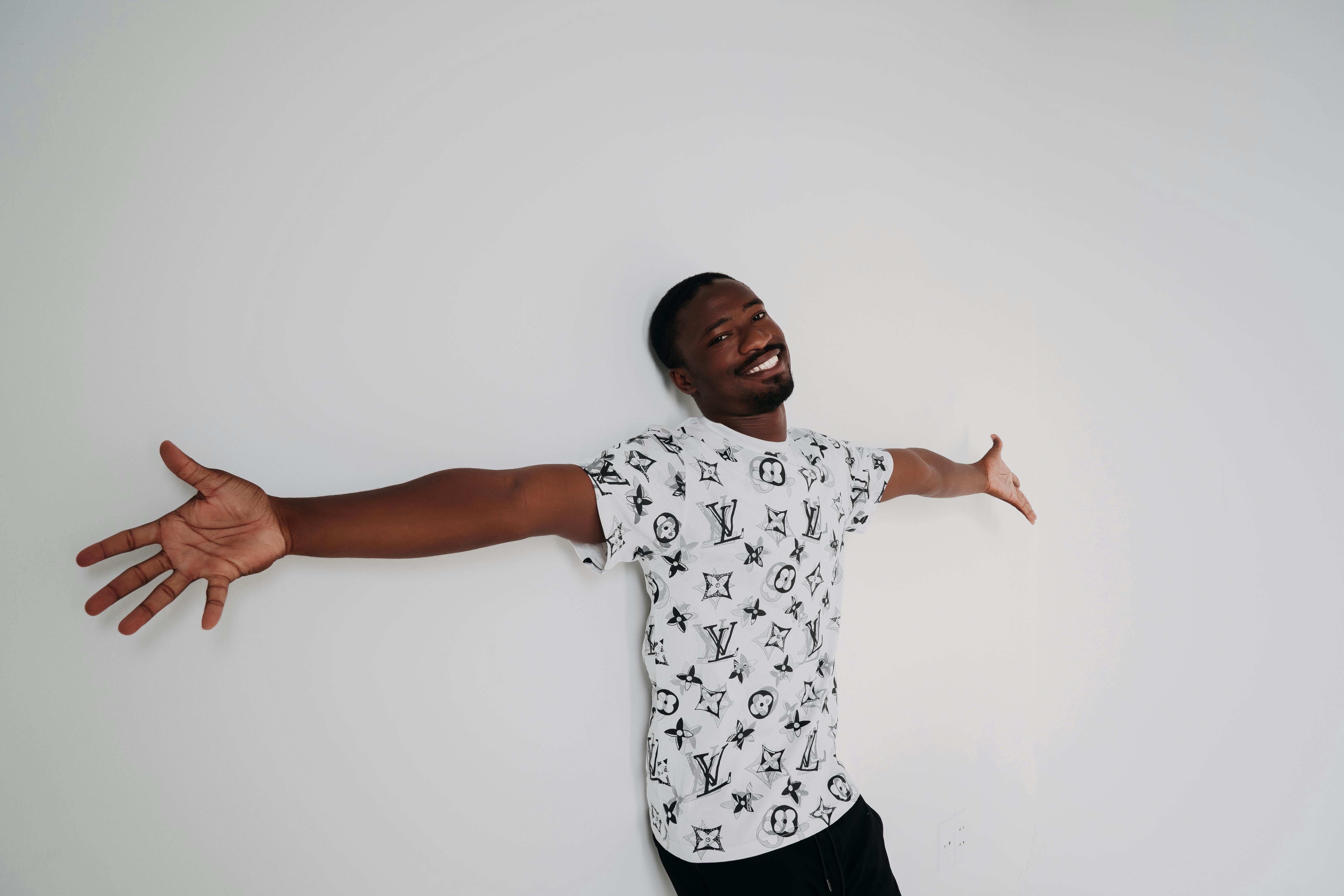 De franc Home somrient amb els braços ben oberts contra una paret blanca, expressant llibertat i alegria. Foto d'estoc