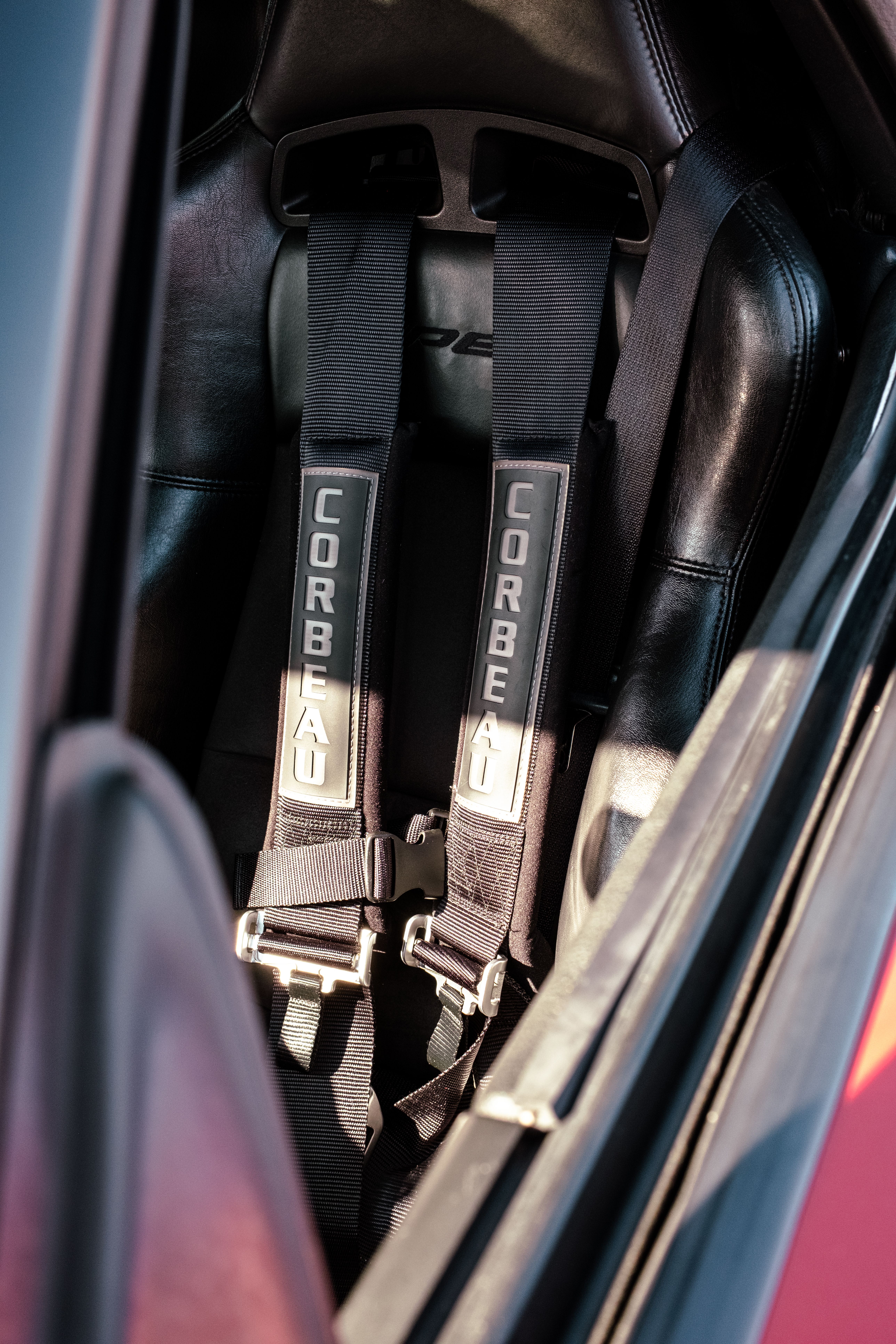 Detailed view of a Corbeau racing seat harness inside a vehicle with natural lighting.