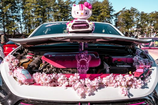 A car hood adorned with Hello Kitty figures and cherry blossoms at a car show.
