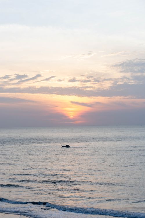 Free A peaceful sunrise over the ocean in Vũng Tàu, Vietnam with a small boat on the horizon. Stock Photo