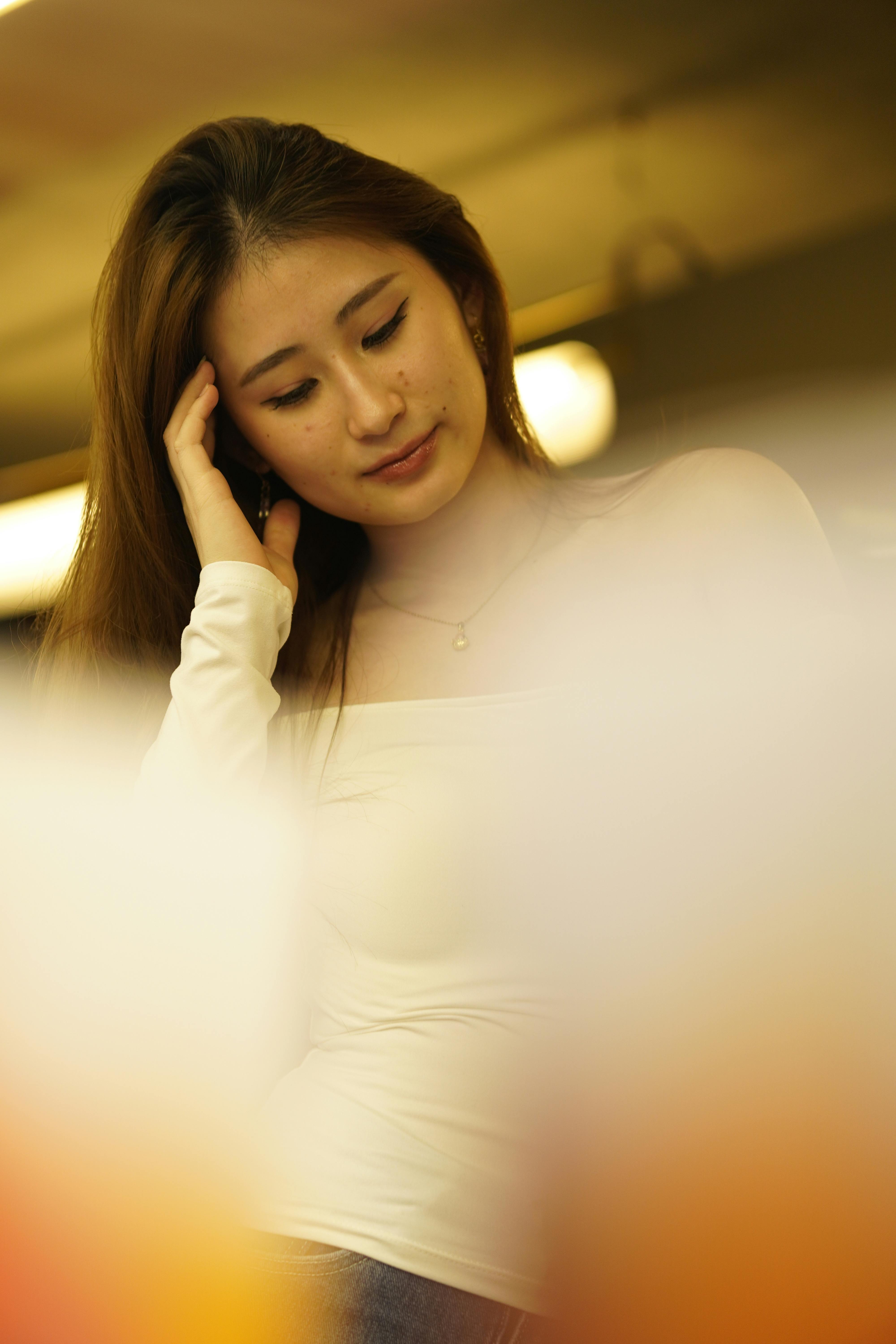 A thoughtful woman with long hair is captured indoors in warm lighting, conveying a serene mood.