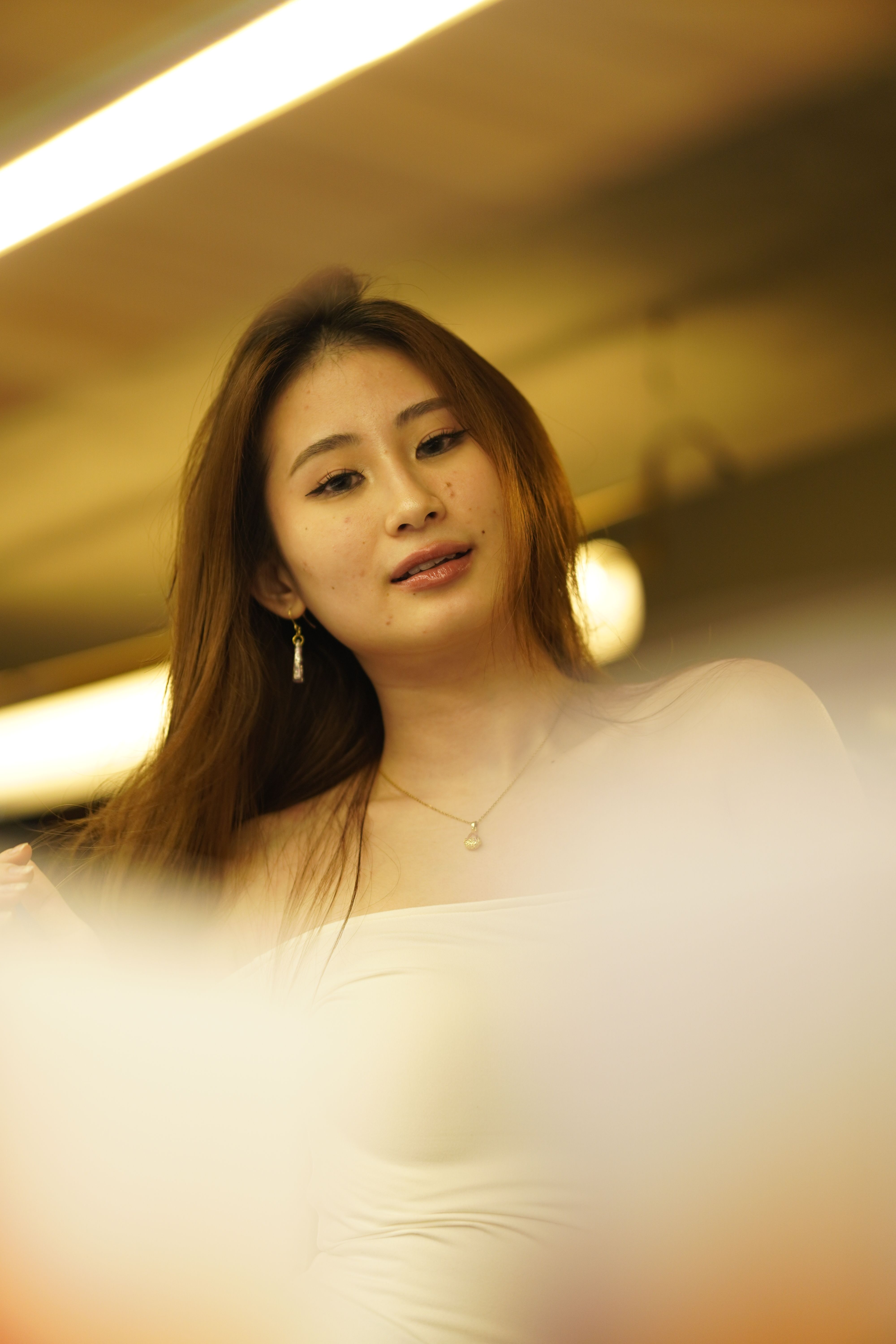 Warm portrait of a woman with long hair and jewelry under indoor lighting, creates a thoughtful mood.