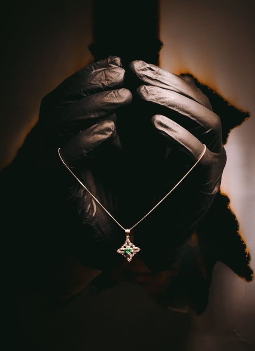 Free A silver necklace with a star pendant held by black gloves in dramatic lighting. Stock Photo