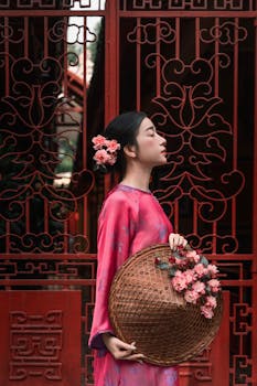 Portrait of a woman in red traditional attire holding a floral basket by a decorative gate.
