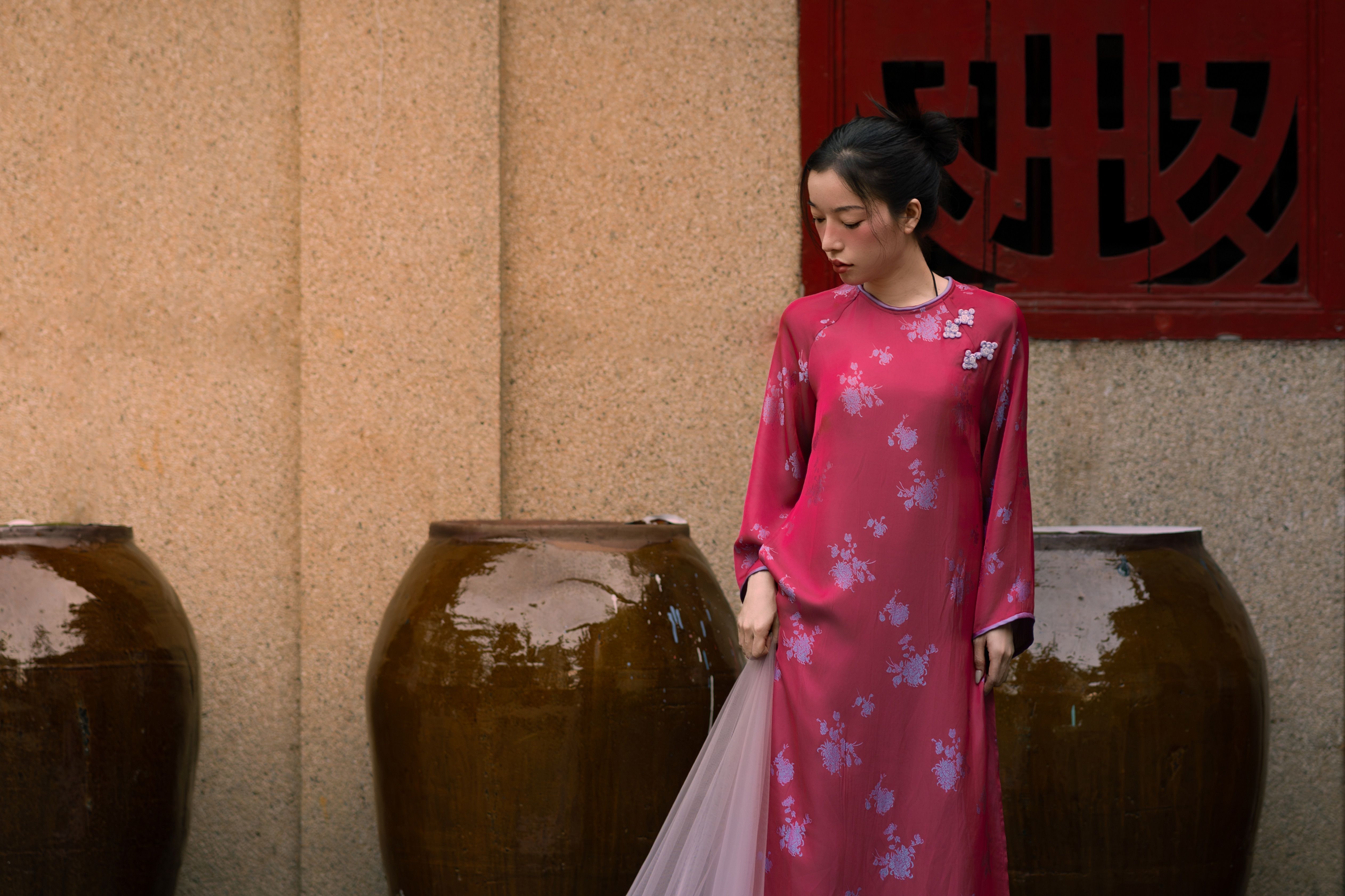 De franc Una dona amb vestit tradicional rosa es troba al costat de grans gerres contra una paret decorativa. Foto d'estoc