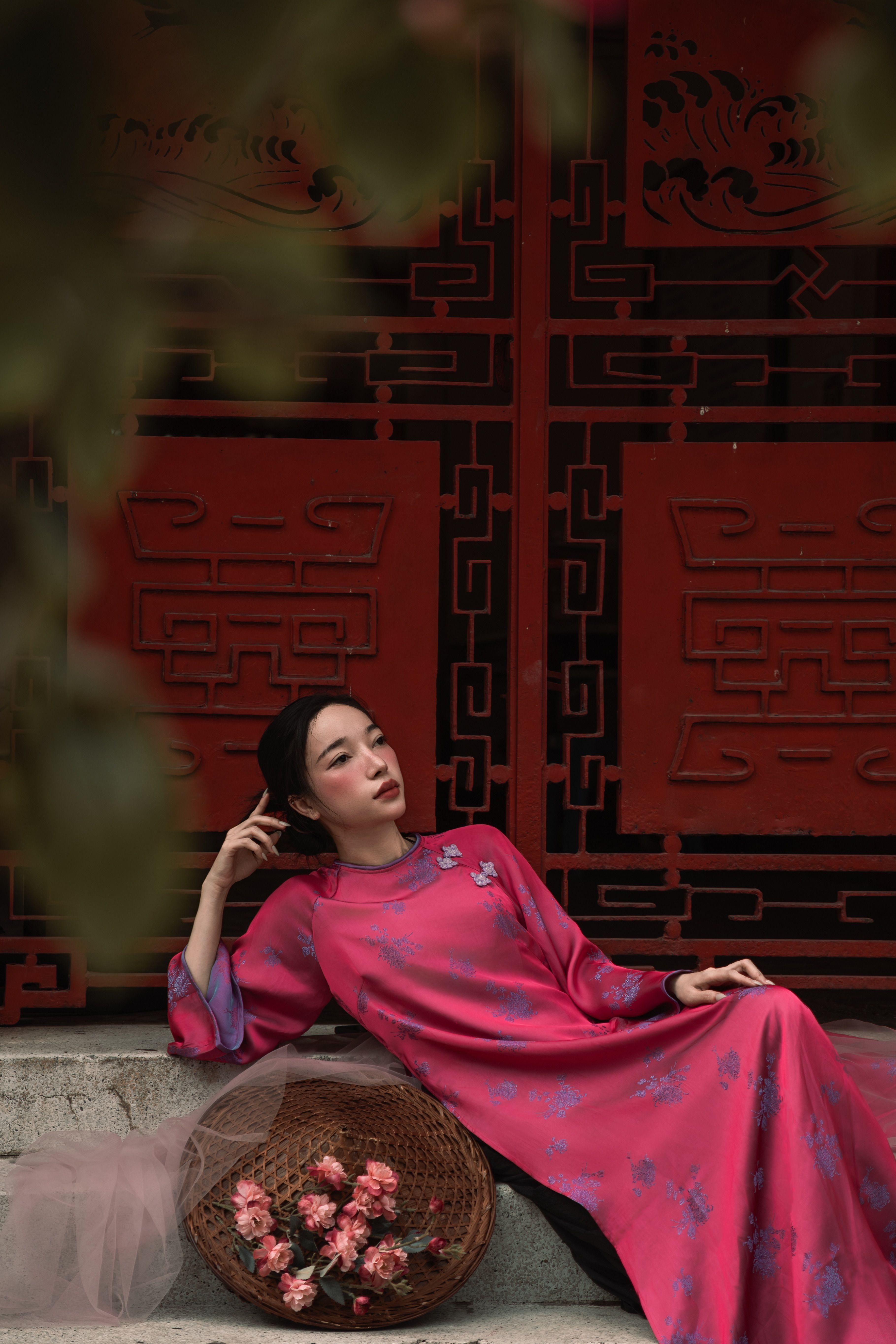 De franc Dona amb vestit tradicional rosa descansant elegantment amb portes ornamentades vermelles al fons. Foto d'estoc