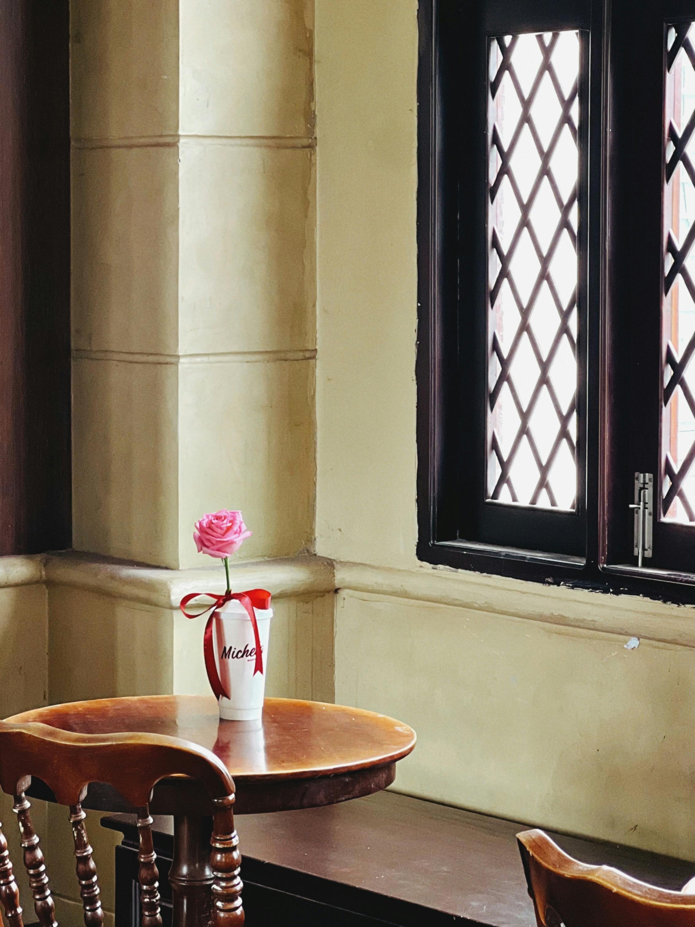 Gratuit Un colț liniștit cu o masă de lemn, un trandafir roz într-o vază și ferestre cu zăbrele. Fotografie de stoc