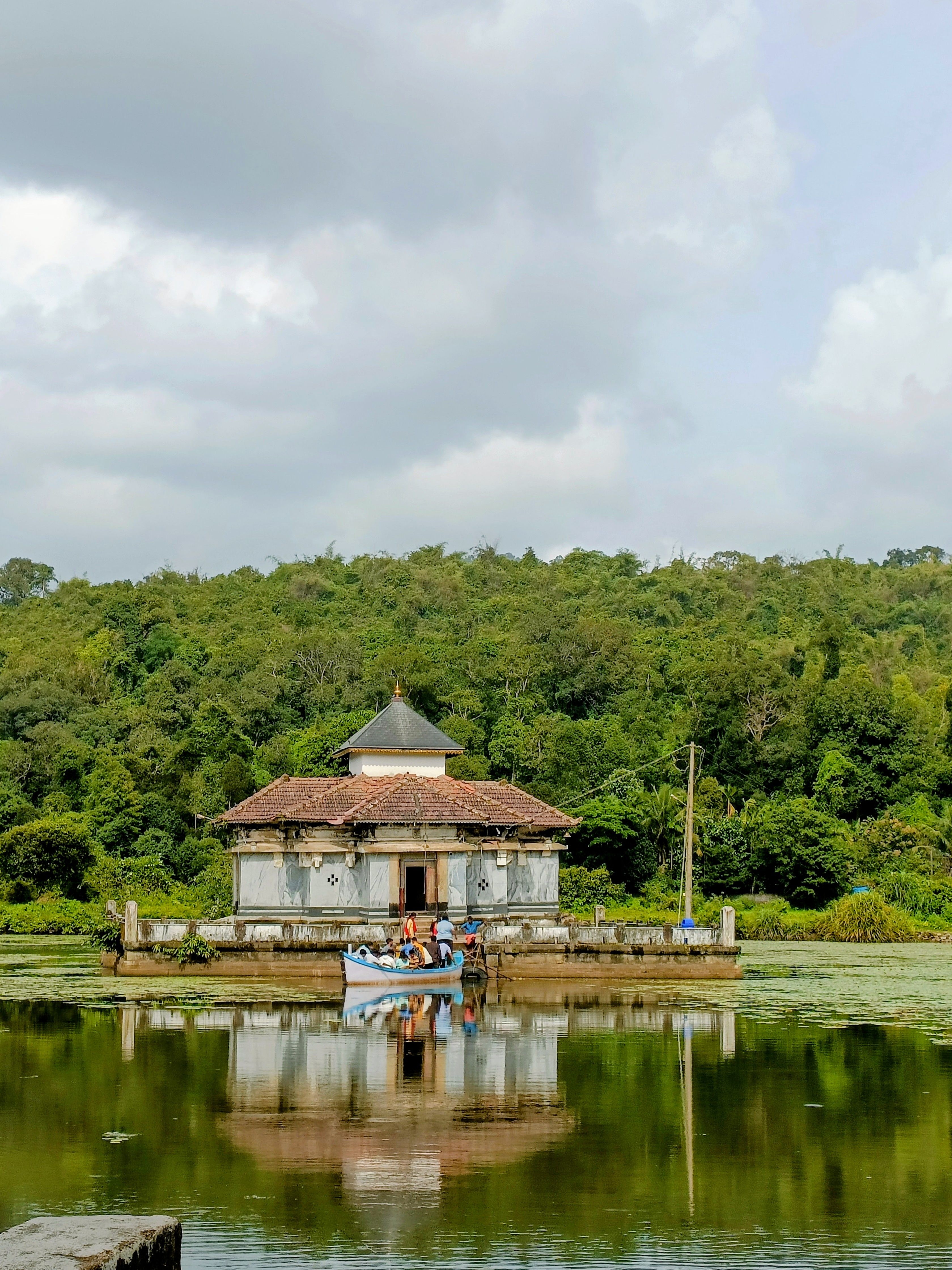 Peaceful temple by a lake amidst lush greenery, mirrored in still waters.