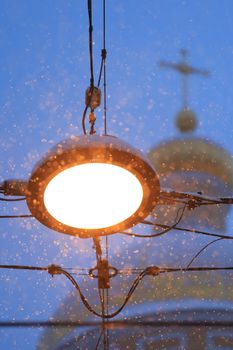 Bright streetlight with snowflakes and blurred golden church dome in winter.