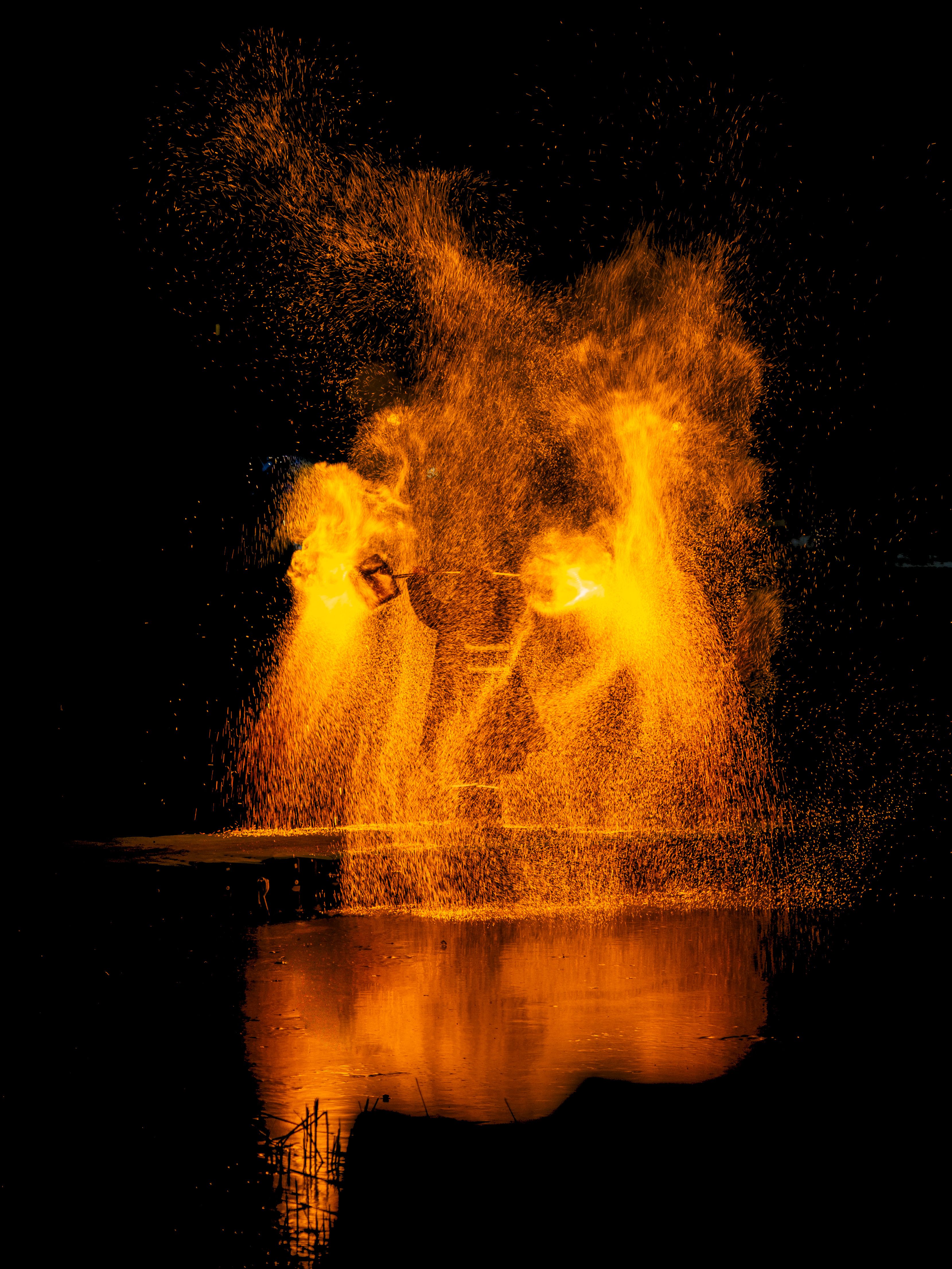 Dramatic night scene of fire performer with vivid sparks and reflection.