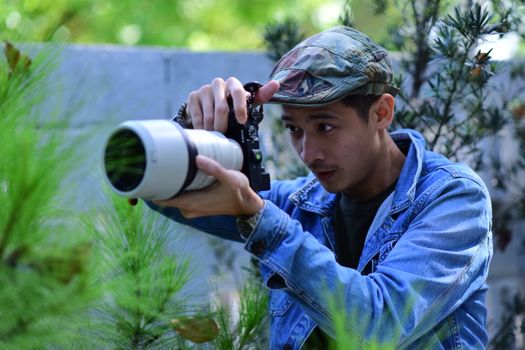 A focused photographer in a camo cap captures nature through a telephoto lens outdoors.