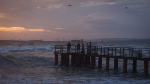 Free Tranquil sunset view of a pier with people against ocean waves and birds. Stock Photo