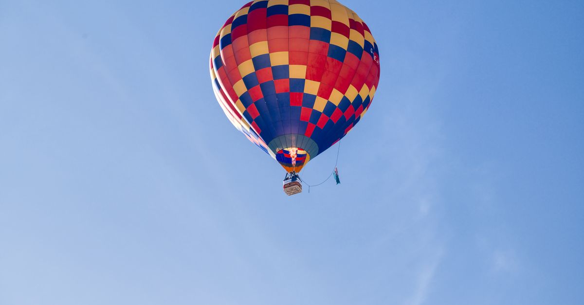 Colorful hot air balloon soaring high against a clear blue sky in Château-d'Oex, Switzerland.