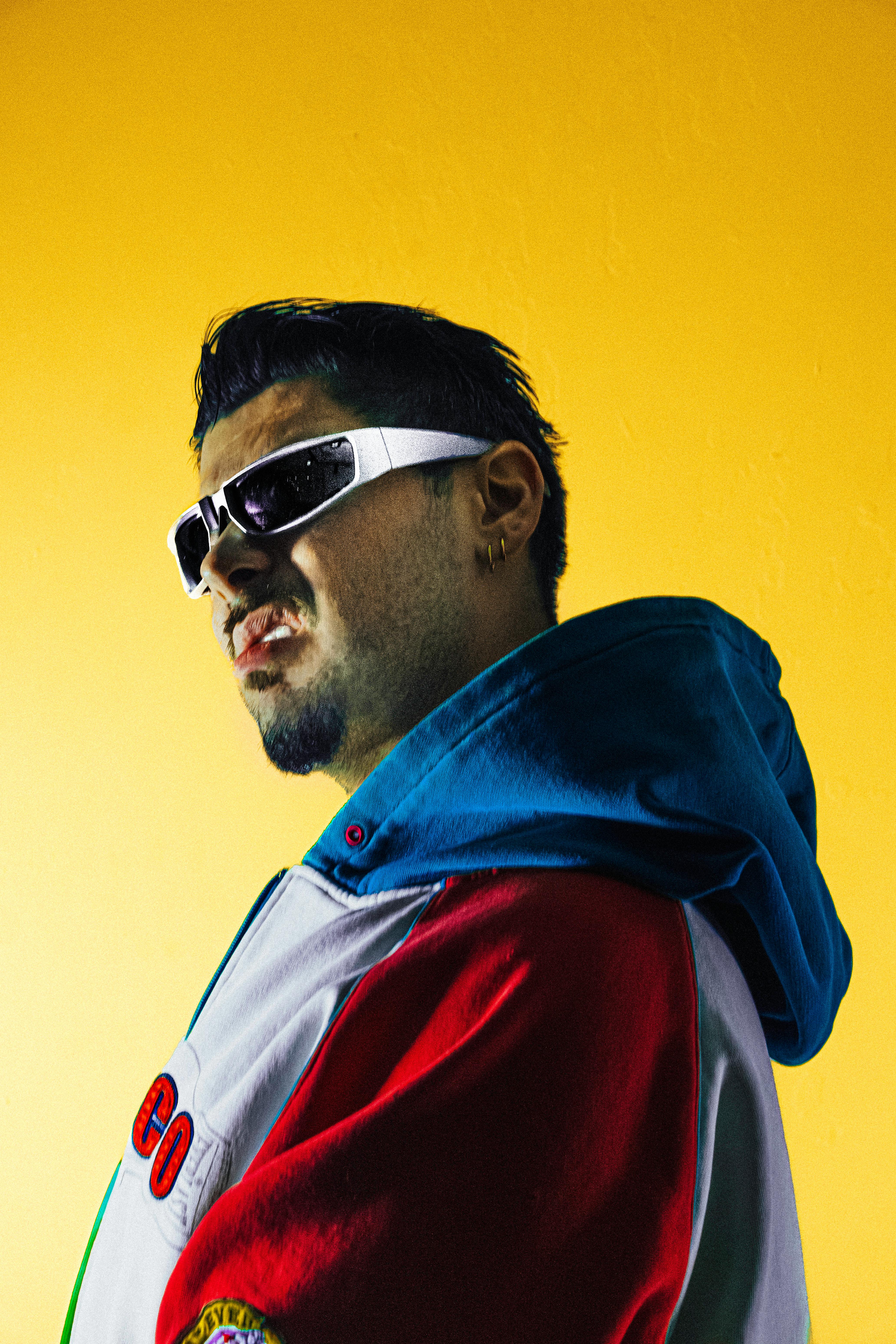Man in sunglasses and colorful jacket poses against a bright yellow background.