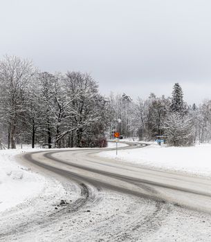 A serene snow-covered road curving through a winter forest on a cloudy day.