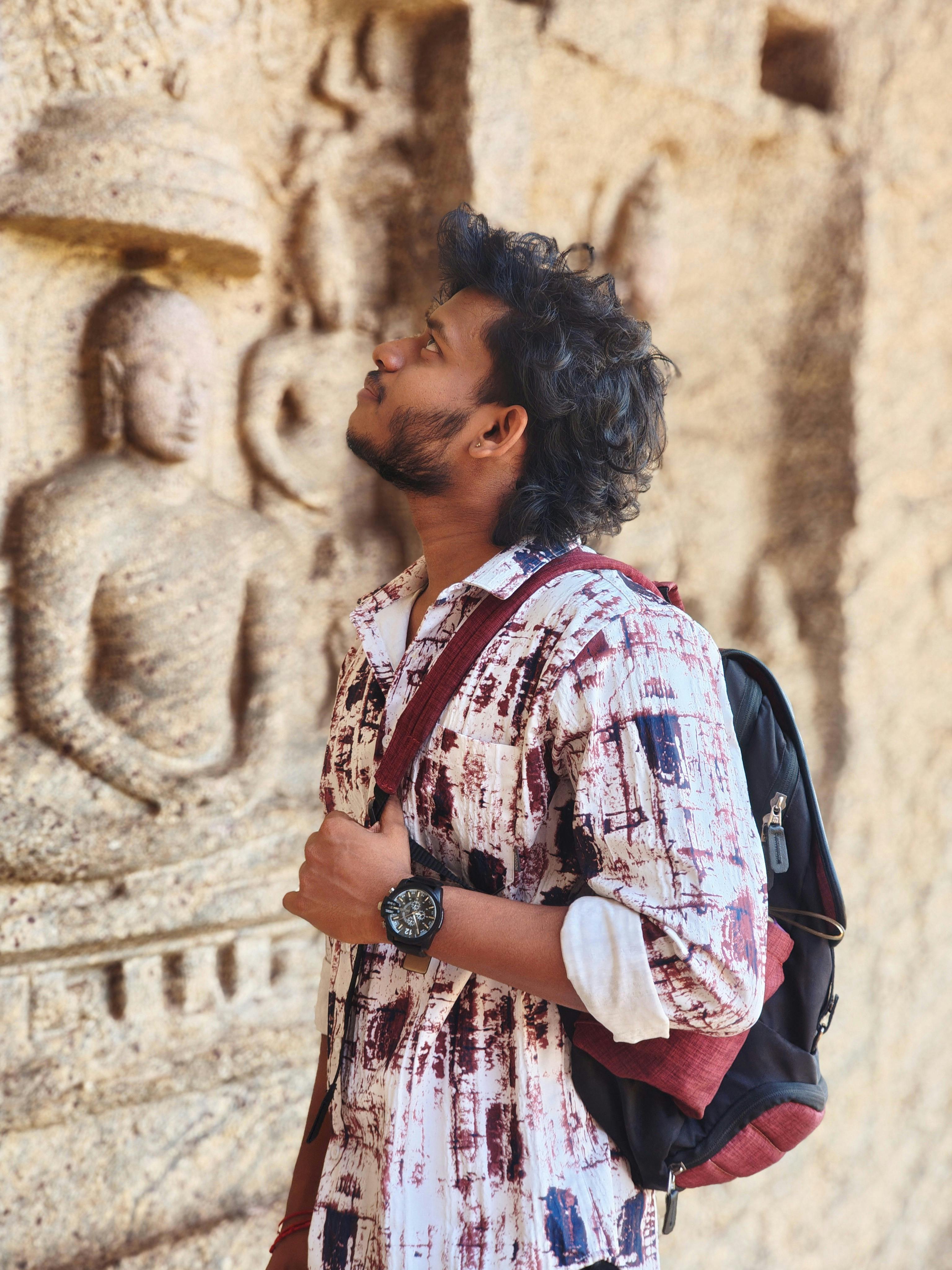 Young man studies intricate stone carvings on an ancient wall, conveying exploration and history.