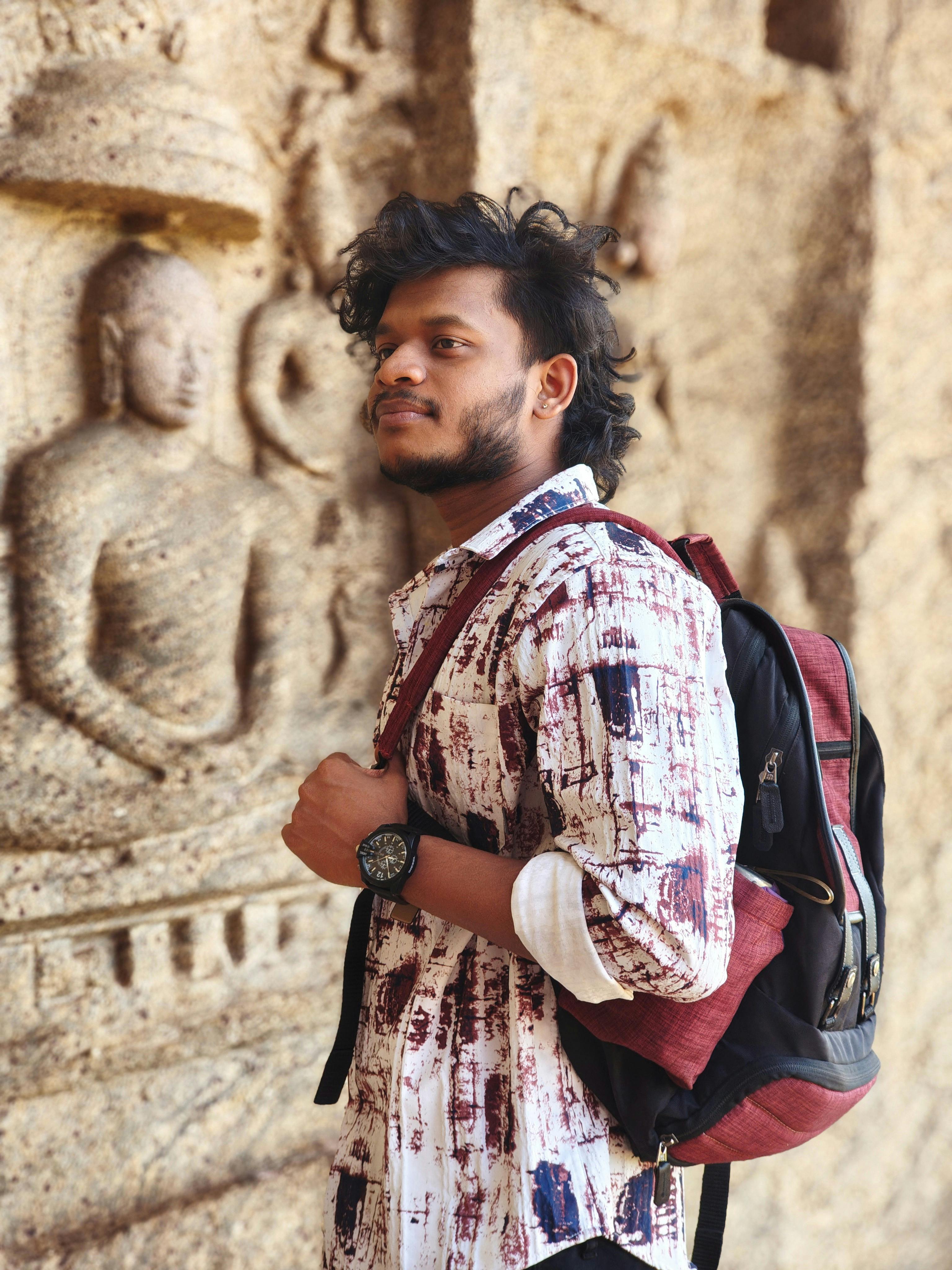Man with backpack admiring ancient stone carvings outdoors.
