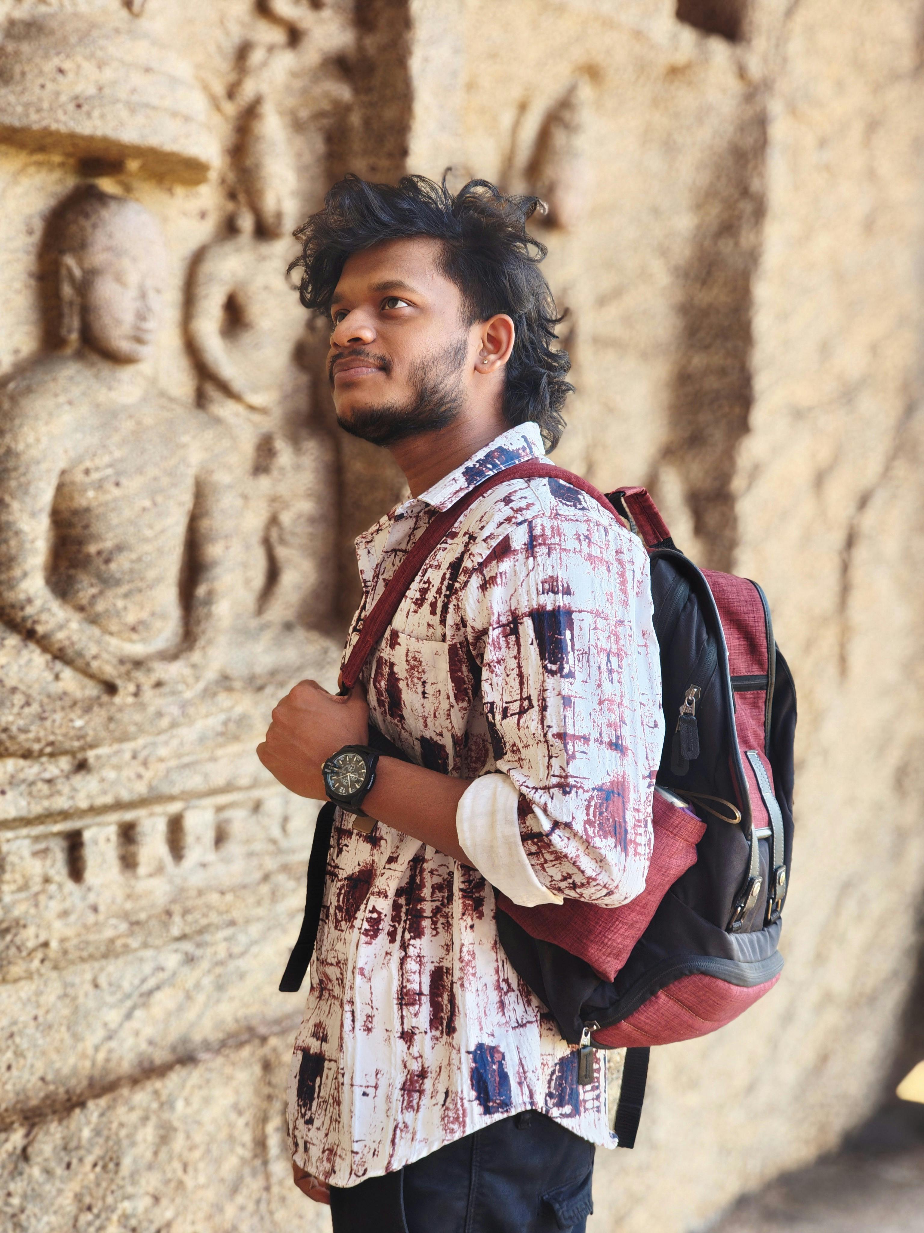 Young man with backpack admiring ancient stone carvings in a historic site.