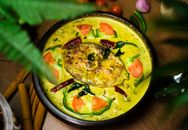 Vibrant Indian fish curry dish garnished with fresh vegetables and spices.
