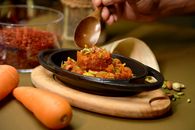 A vibrant Gajar Halwa garnished with pistachios, served in a black dish with carrots and saffron.