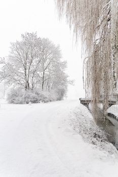 Peaceful winter scene of trees and bridge covered in snow.