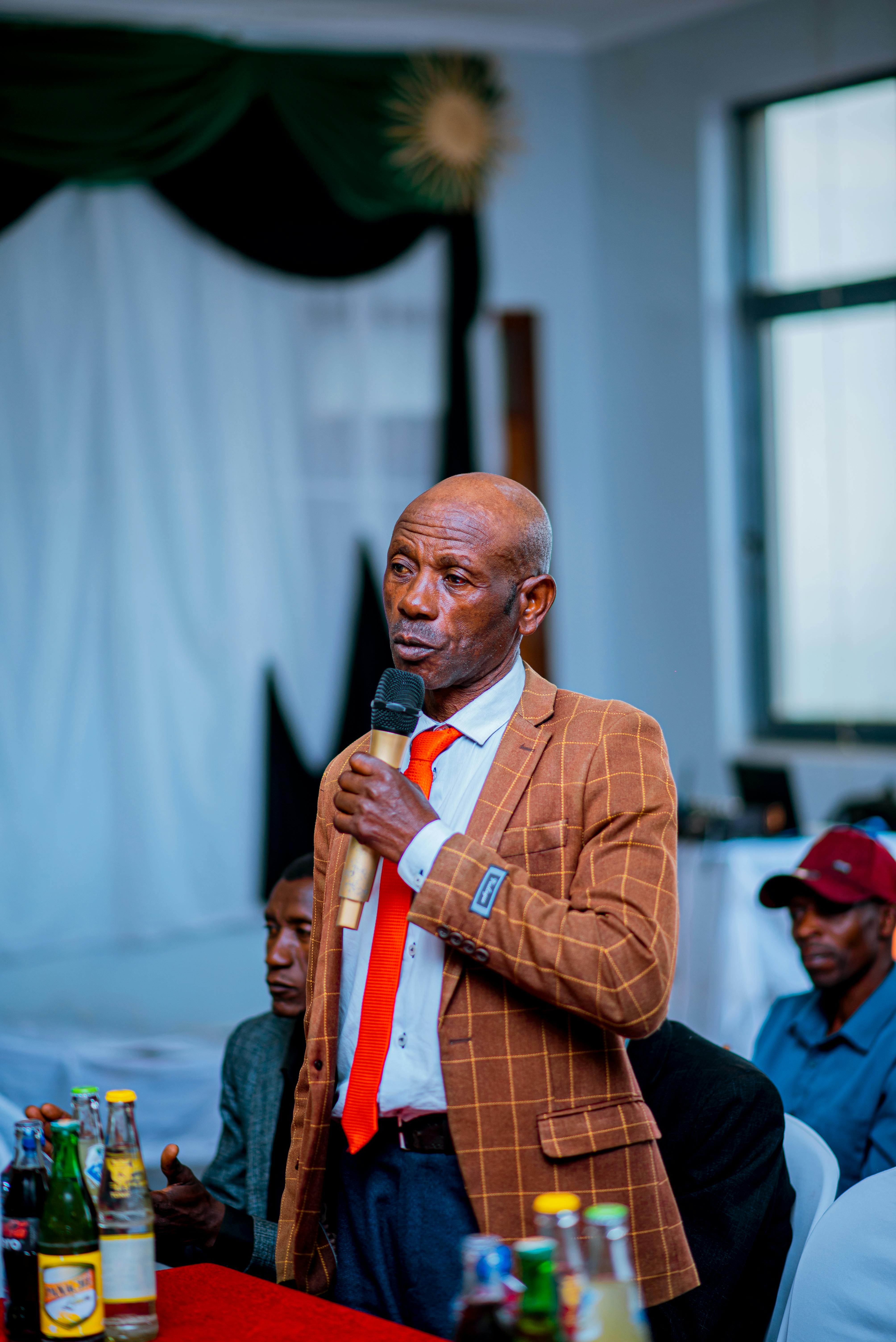 Elderly gentleman giving a speech at an indoor event, elegantly dressed.