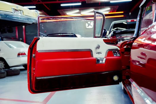 Vintage red and white car door in a garage, highlighting classic automotive design.