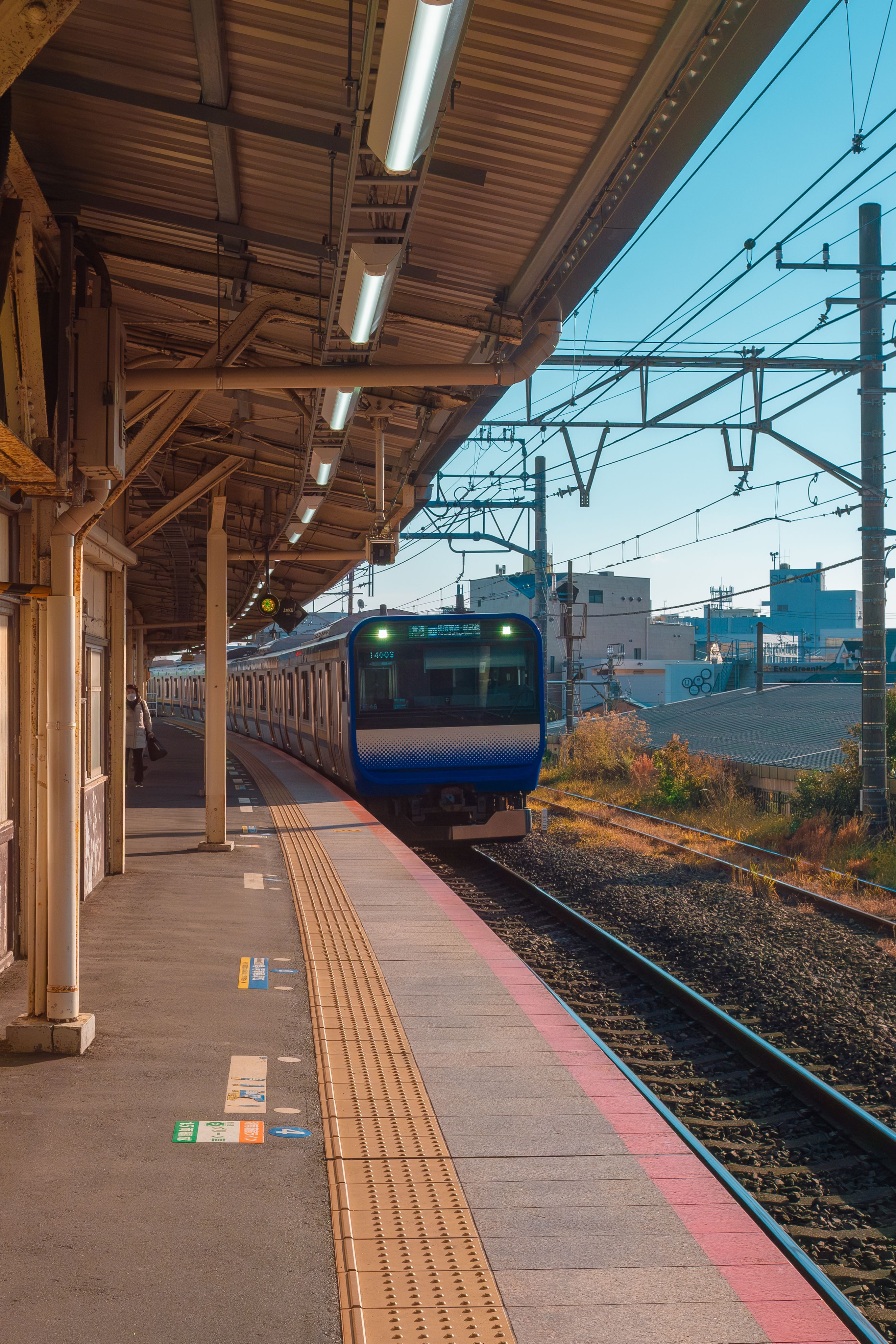 A blue commuter train arrives at an empty outdoor station on a sunny day.