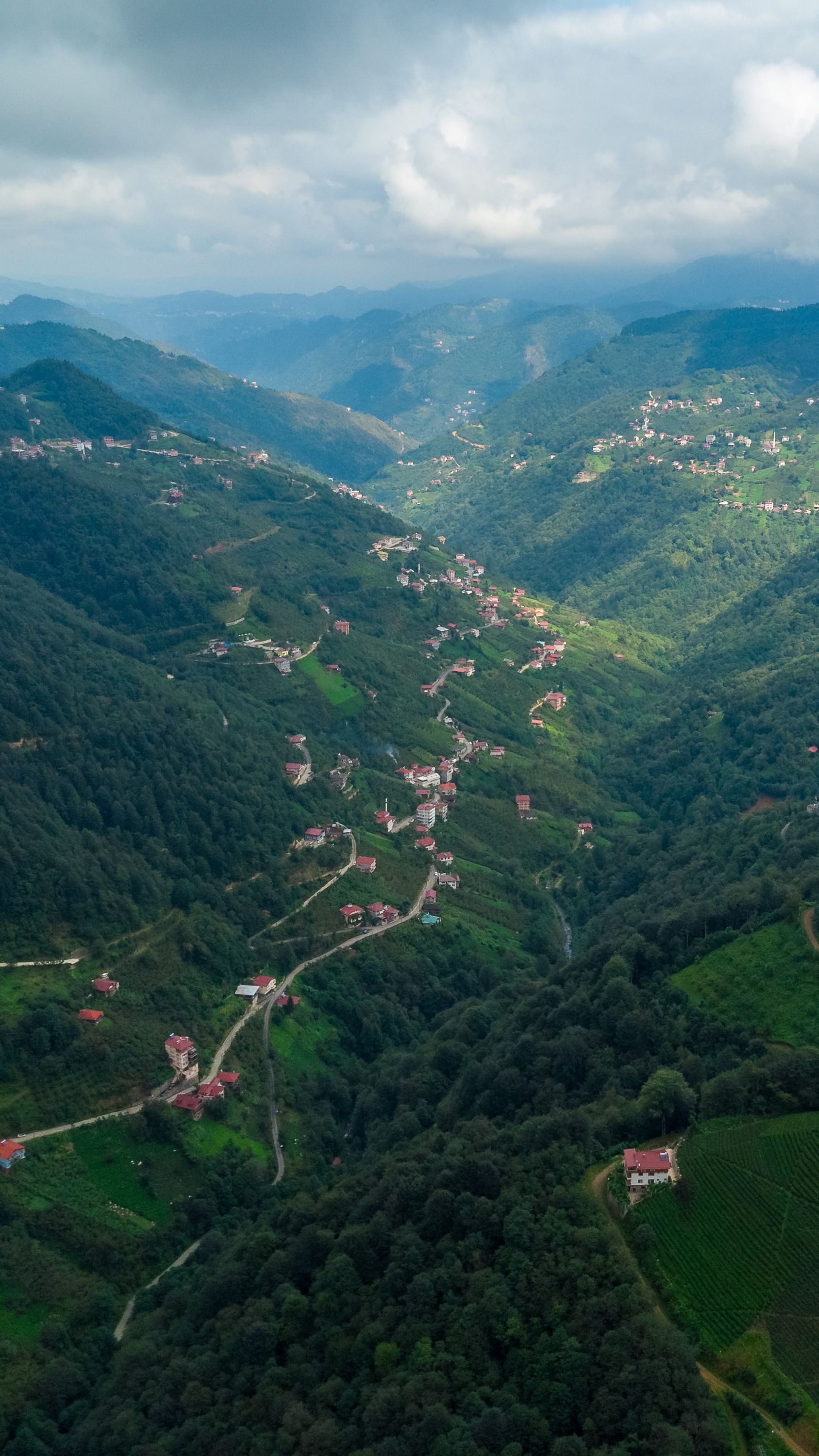Stunning aerial shot of a green mountain valley with scattered villages under dramatic clouds.