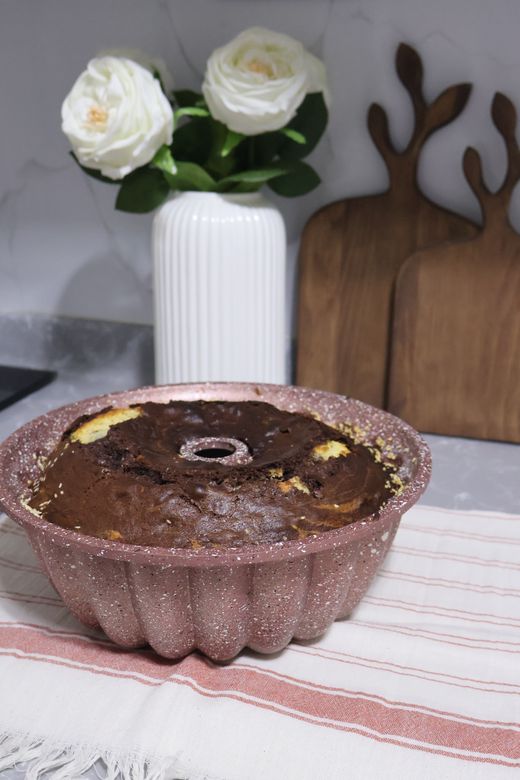 Speckled pink fluted bundt pan holding marble cake on striped towel