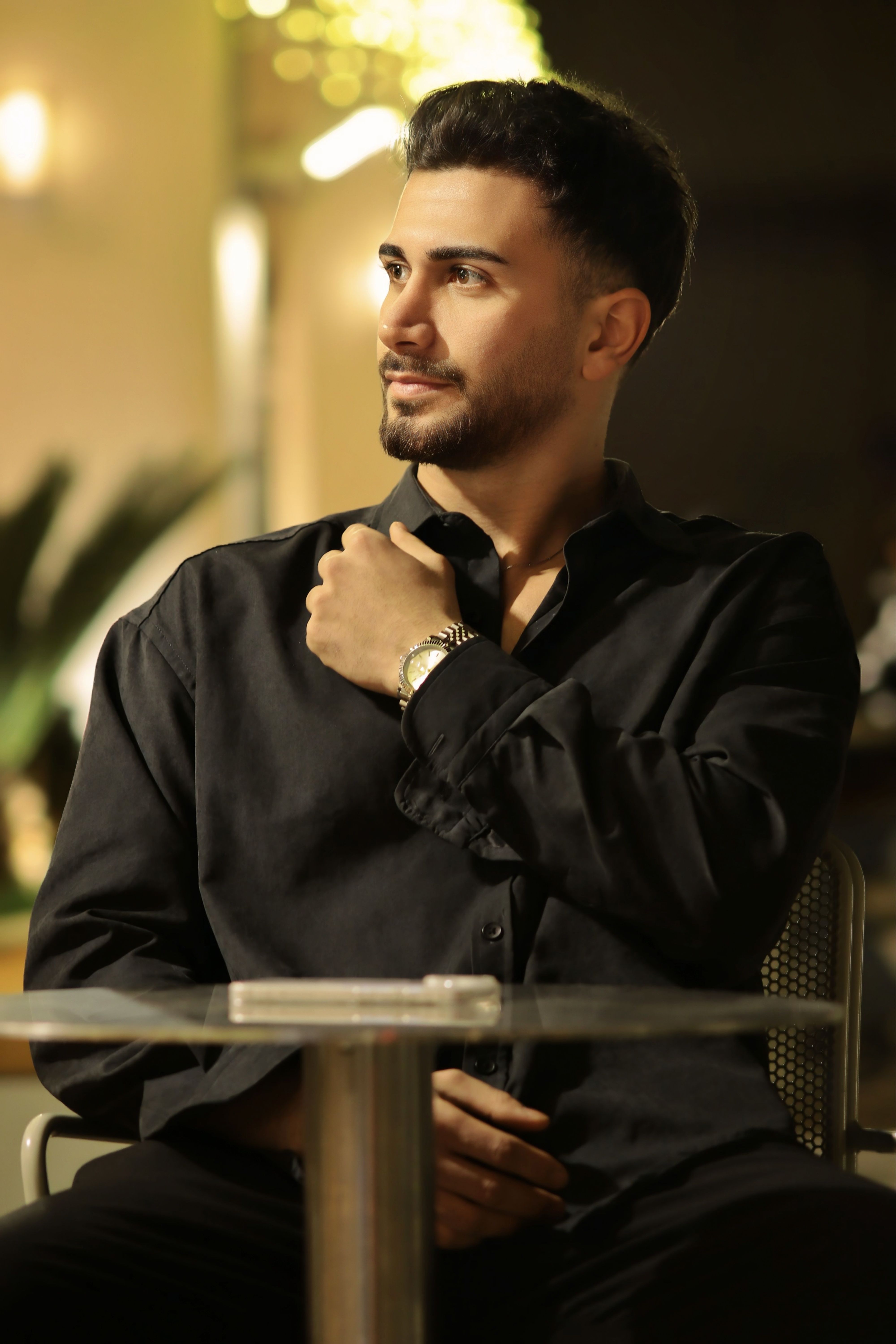 Man in a black shirt sitting at a cafe during the night with a thoughtful look.