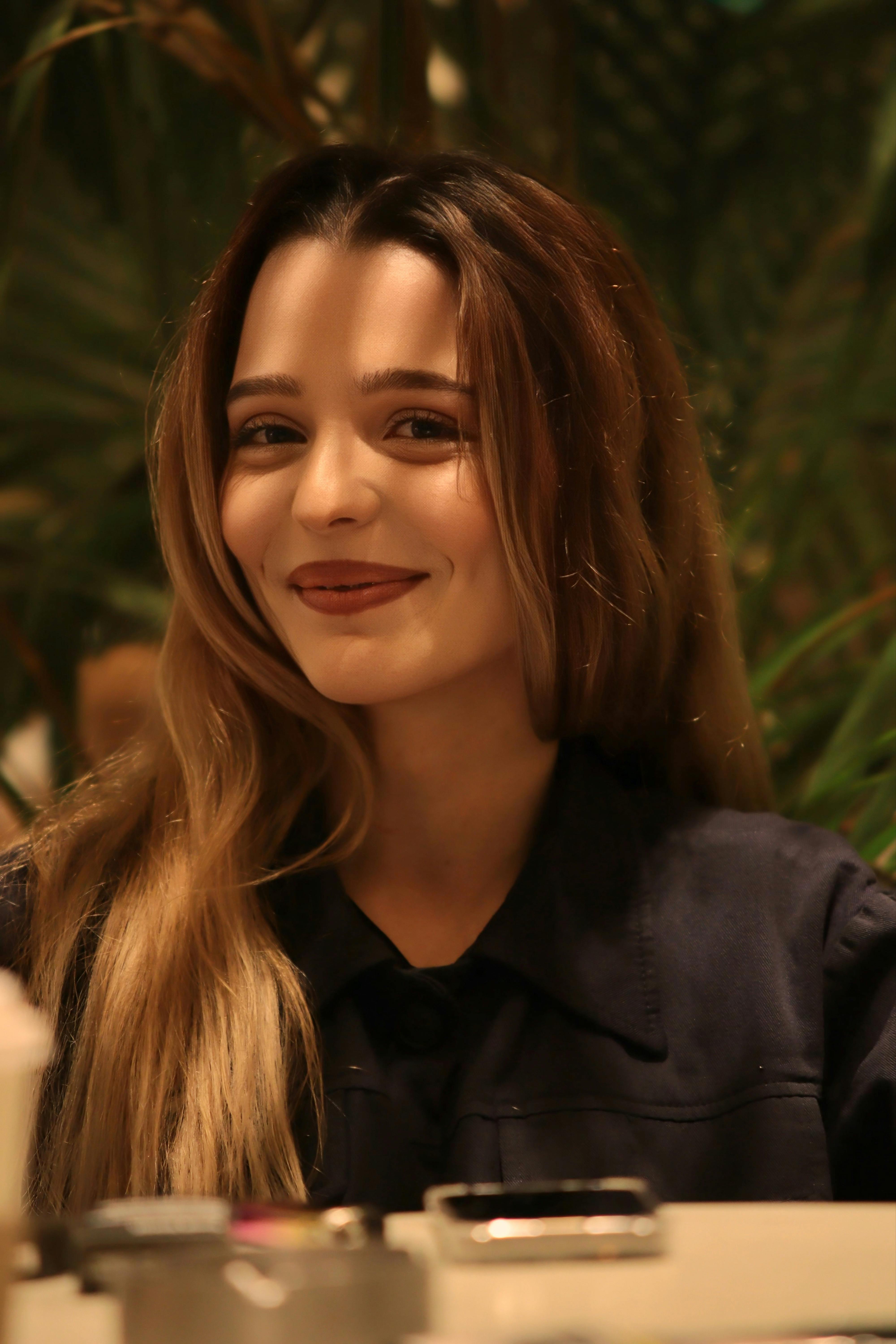 Portrait of a woman with long hair smiling warmly indoors with a soft focus background.
