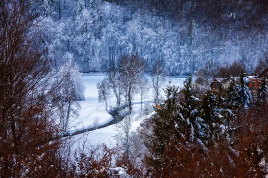 A tranquil winter scene showcasing a snowy Slovenian landscape with frosted trees and a frozen river.