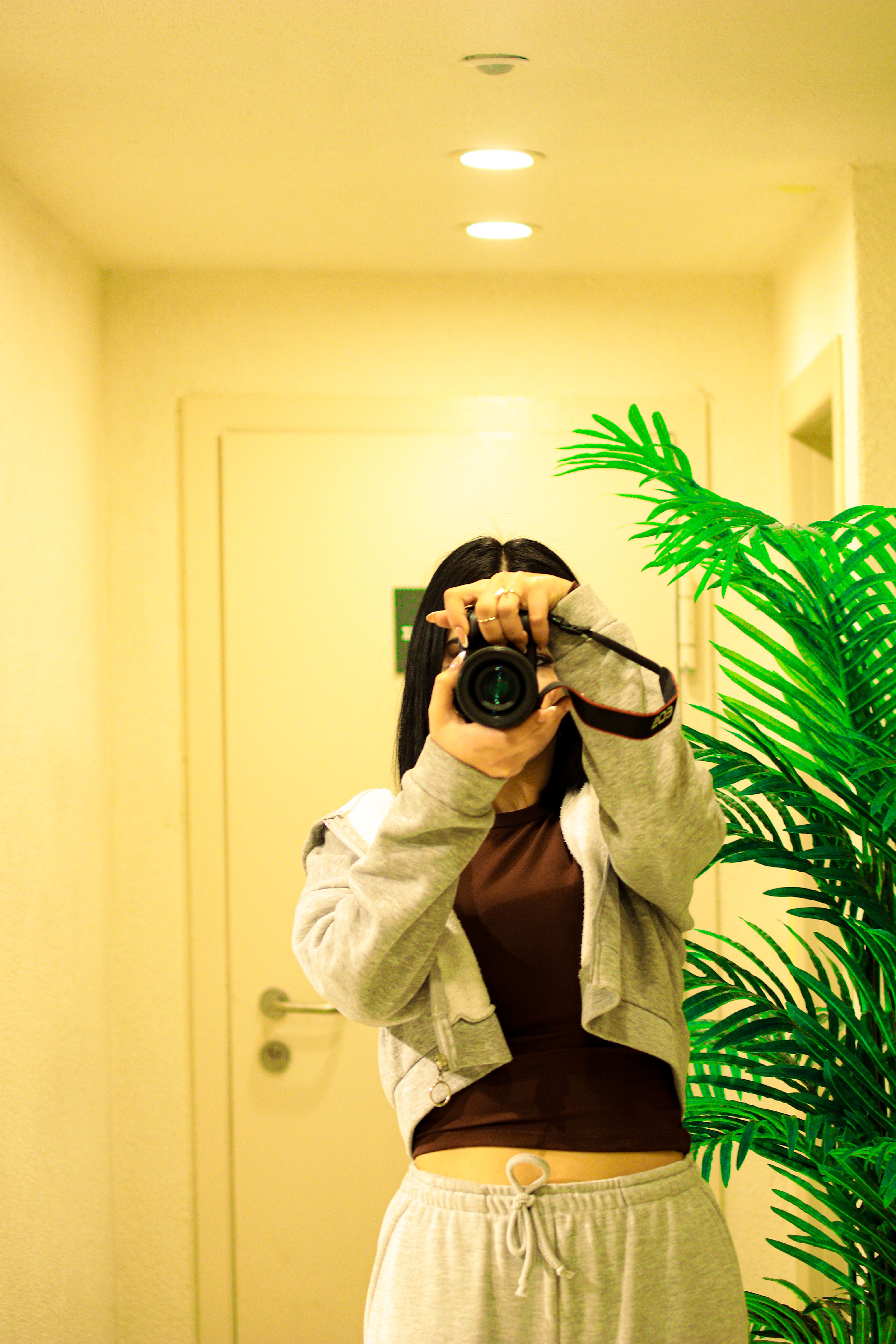 A woman captures a mirror selfie with a camera in a modern indoor setting.