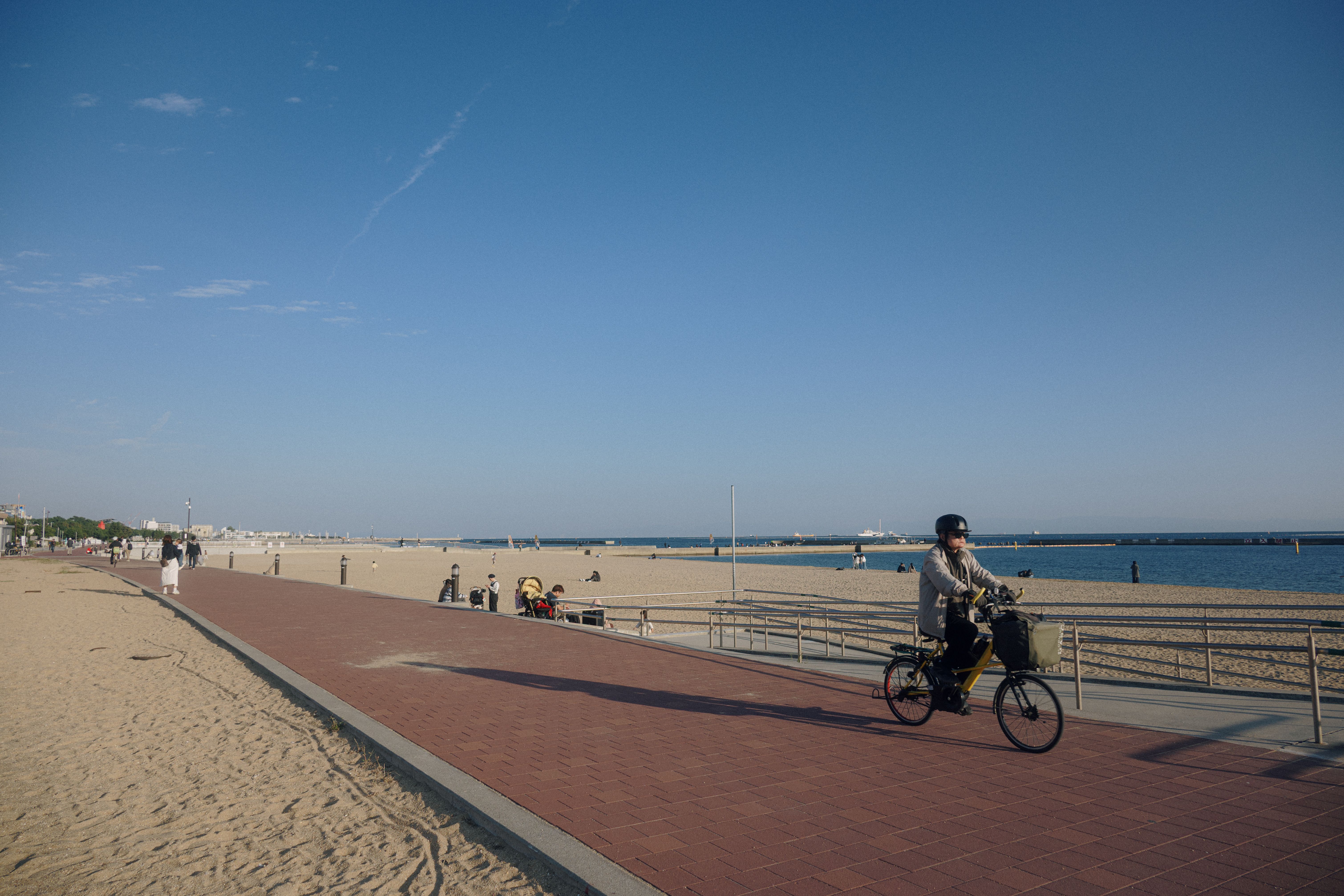 A leisurely cyclist rides by a sandy beach under a clear blue sky, ideal for summer leisure. — Trójmiasto
