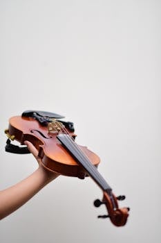 Close-up of a violin held by a child against a plain background, focus on instrument details.