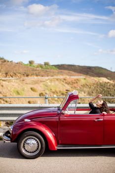 A woman enjoys a drive in a red vintage convertible against a scenic backdrop, capturing a carefree adventure.