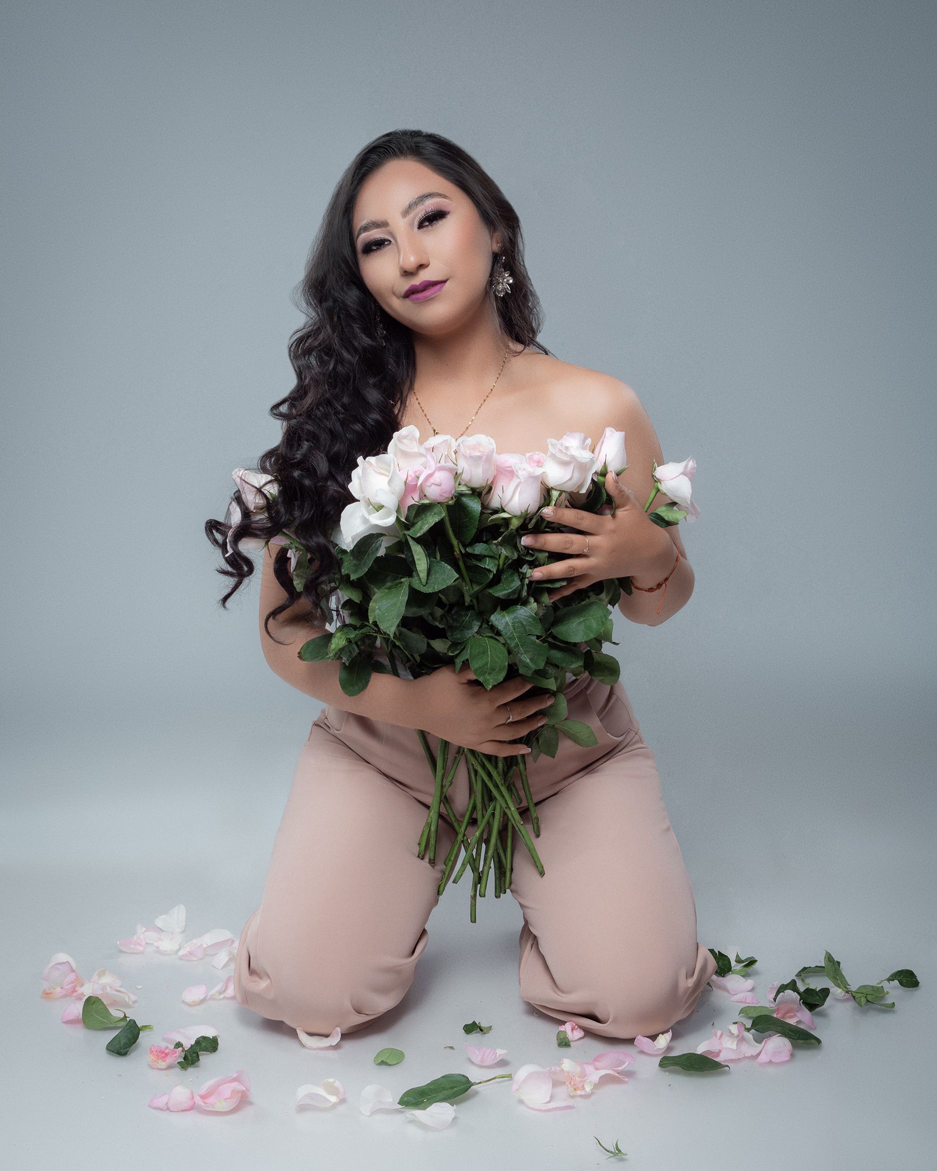 Beautiful woman kneeling with pink and white roses on a studio background.